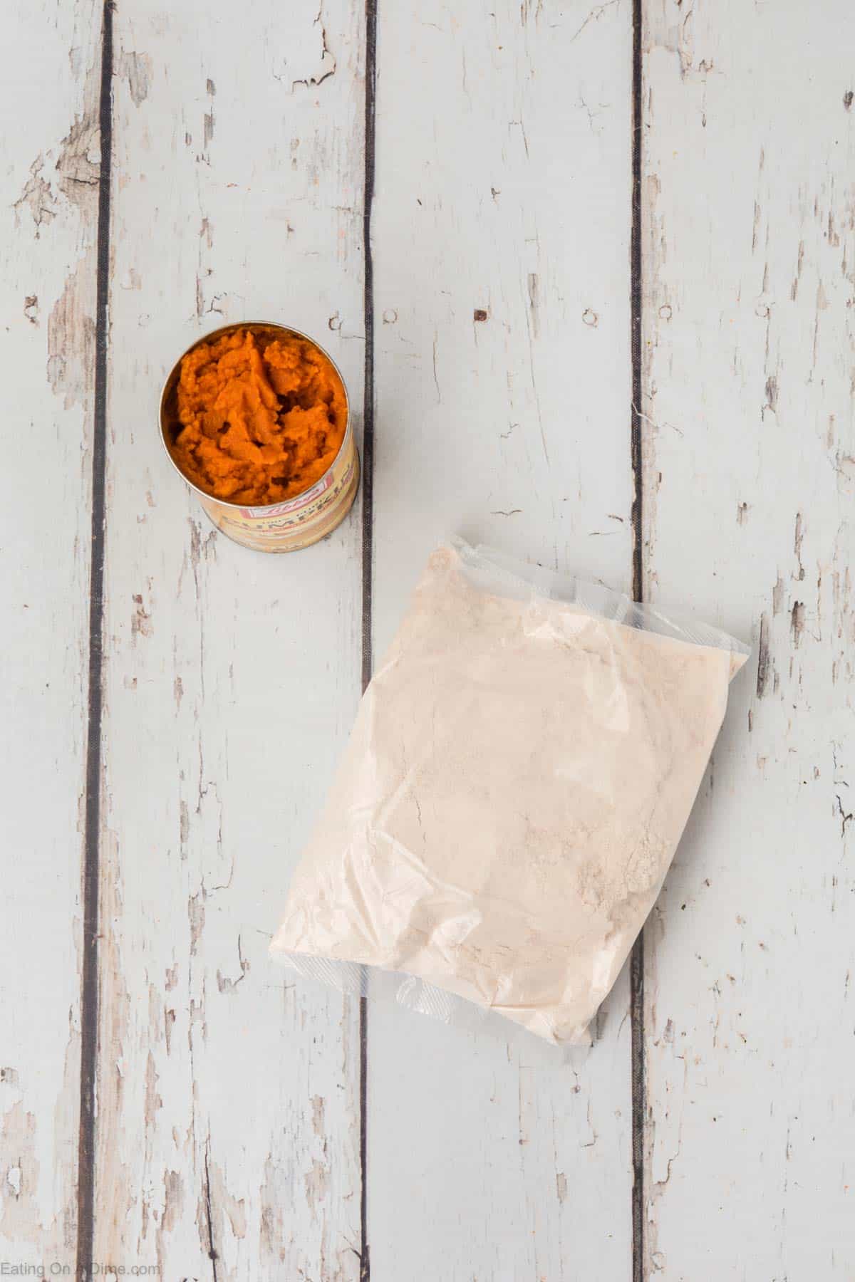 An open can of pumpkin puree and a sealed plastic bag of dry ingredients sit on a rustic wooden surface, hinting at the simplicity of 2 Ingredient Pumpkin Muffins. The dry ingredients appear to be a powder or flour mix, possibly for baking these easy treats.