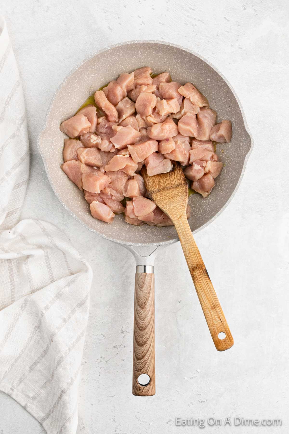 Cooking diced chicken in a large skillet with a wooden spoon