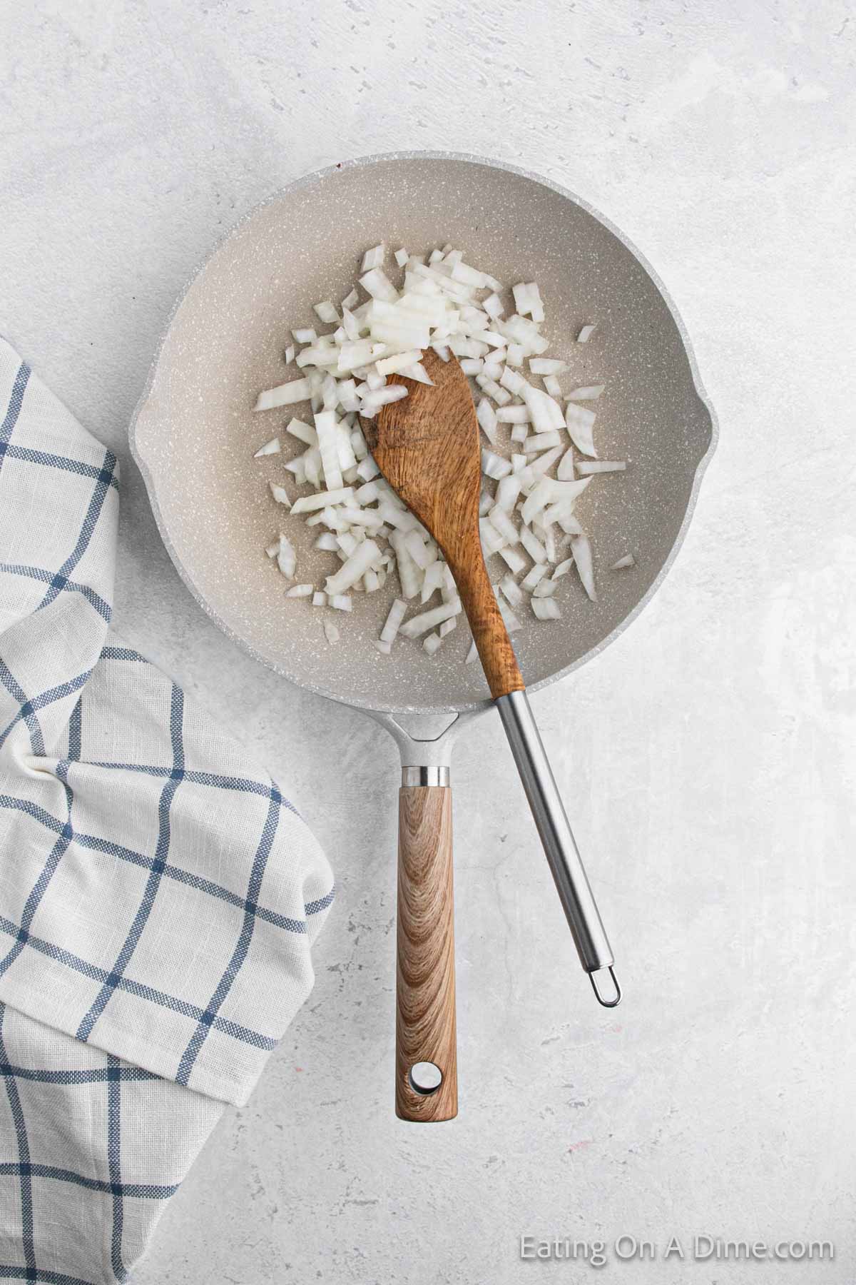Cooking diced onions in a skillet with a wooden spoon