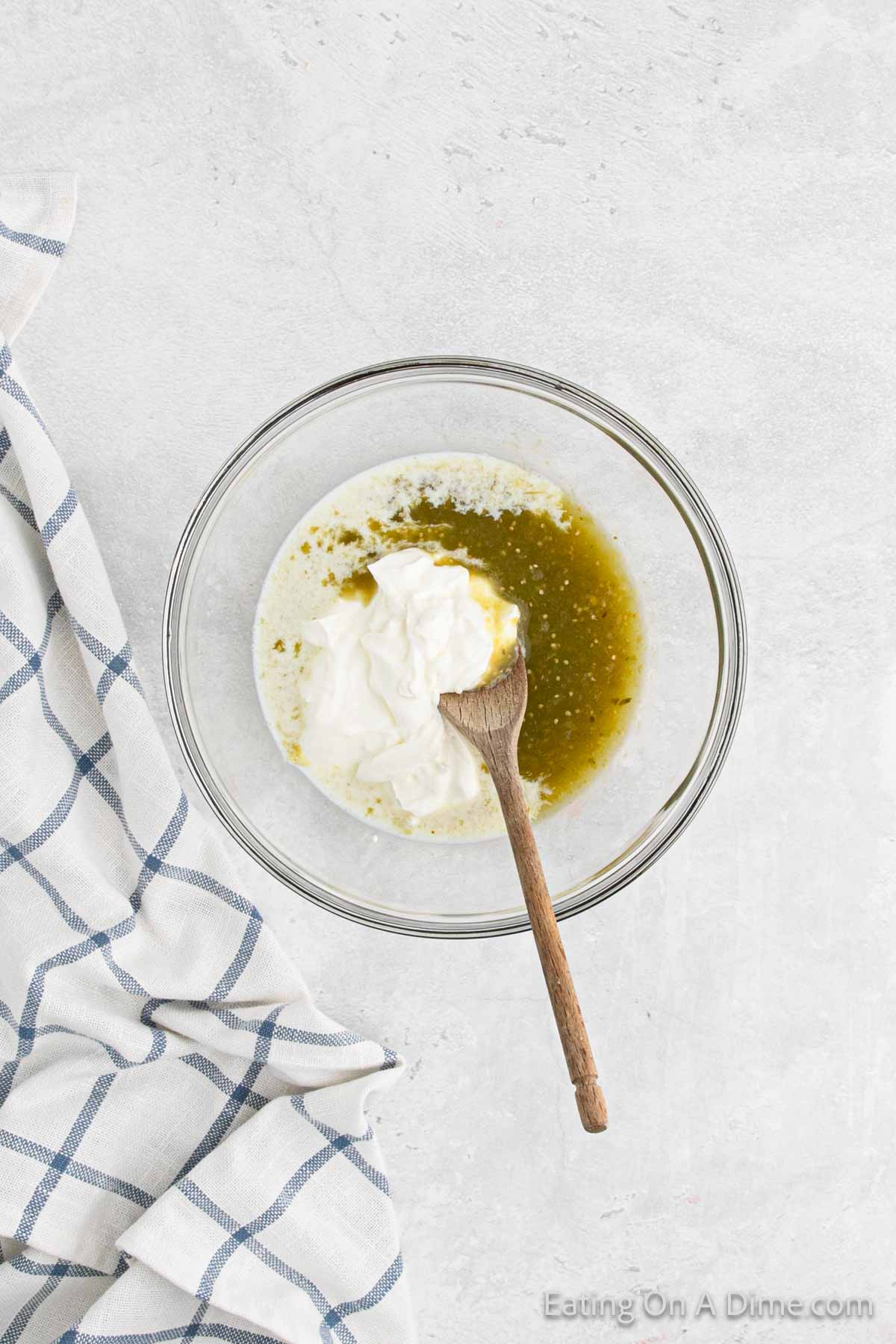 Combining salsa verde, sour cream and milk in a bowl with a wooden spoon