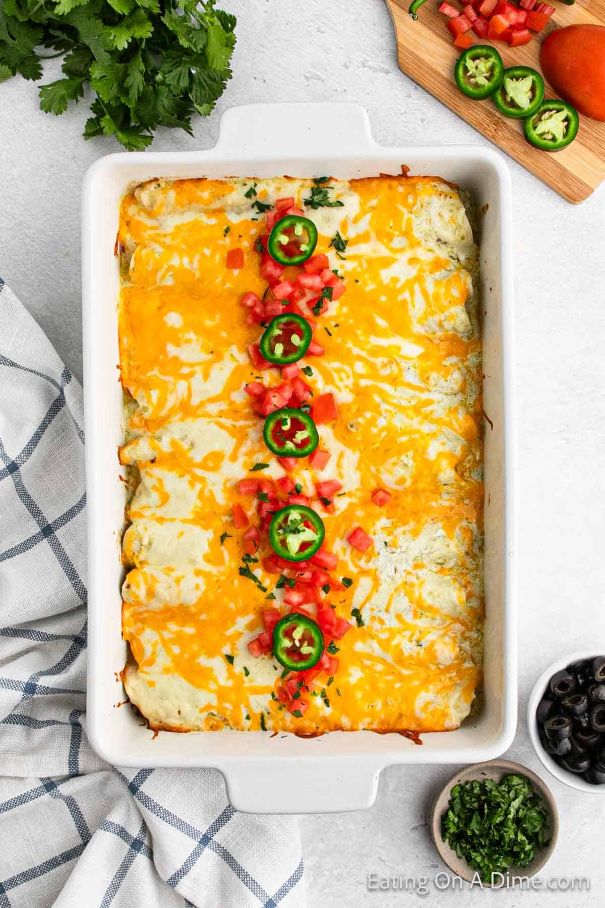 Green chili enchiladas in a baking dish topped with diced tomatoes and slice jalapenos