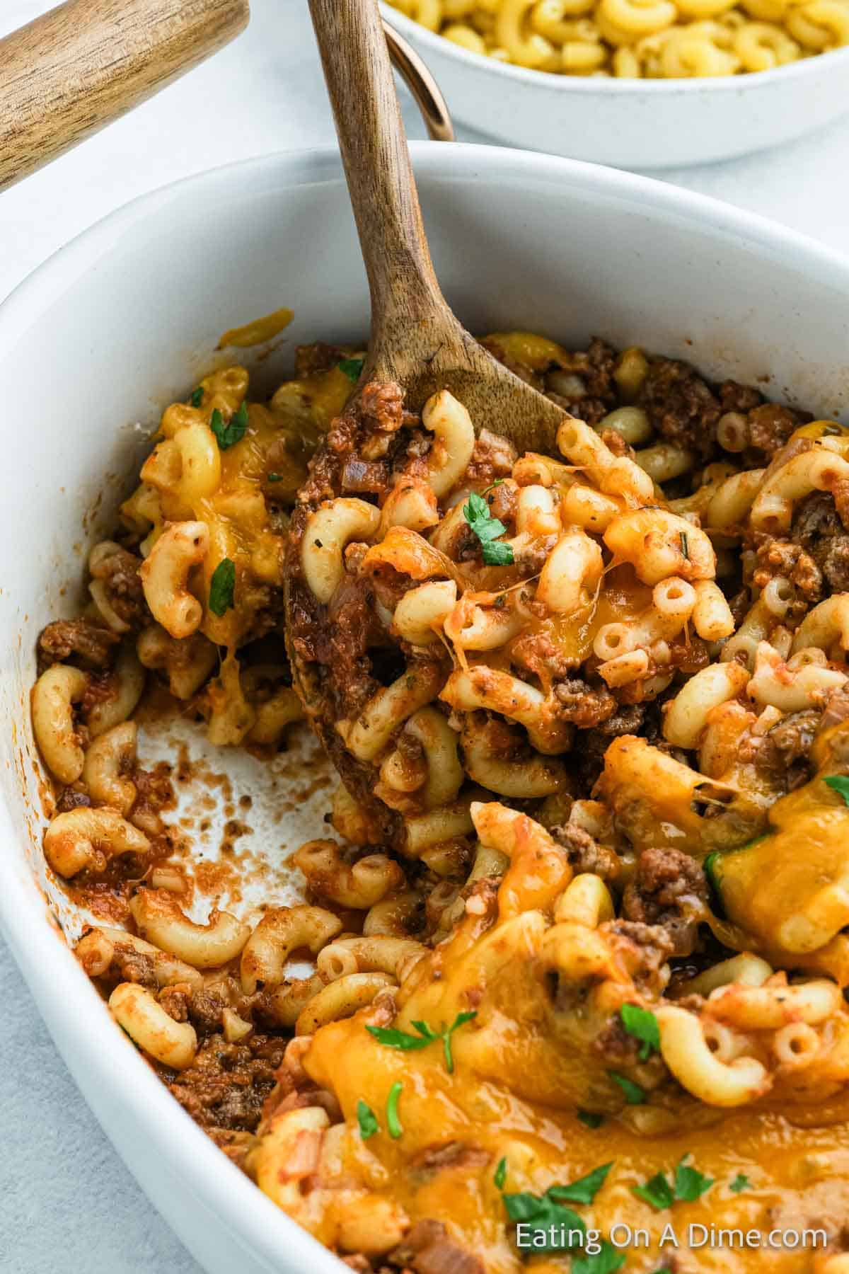 Hamburger Casserole in a casserole dish with a wooden spoon and topped with melted cheese