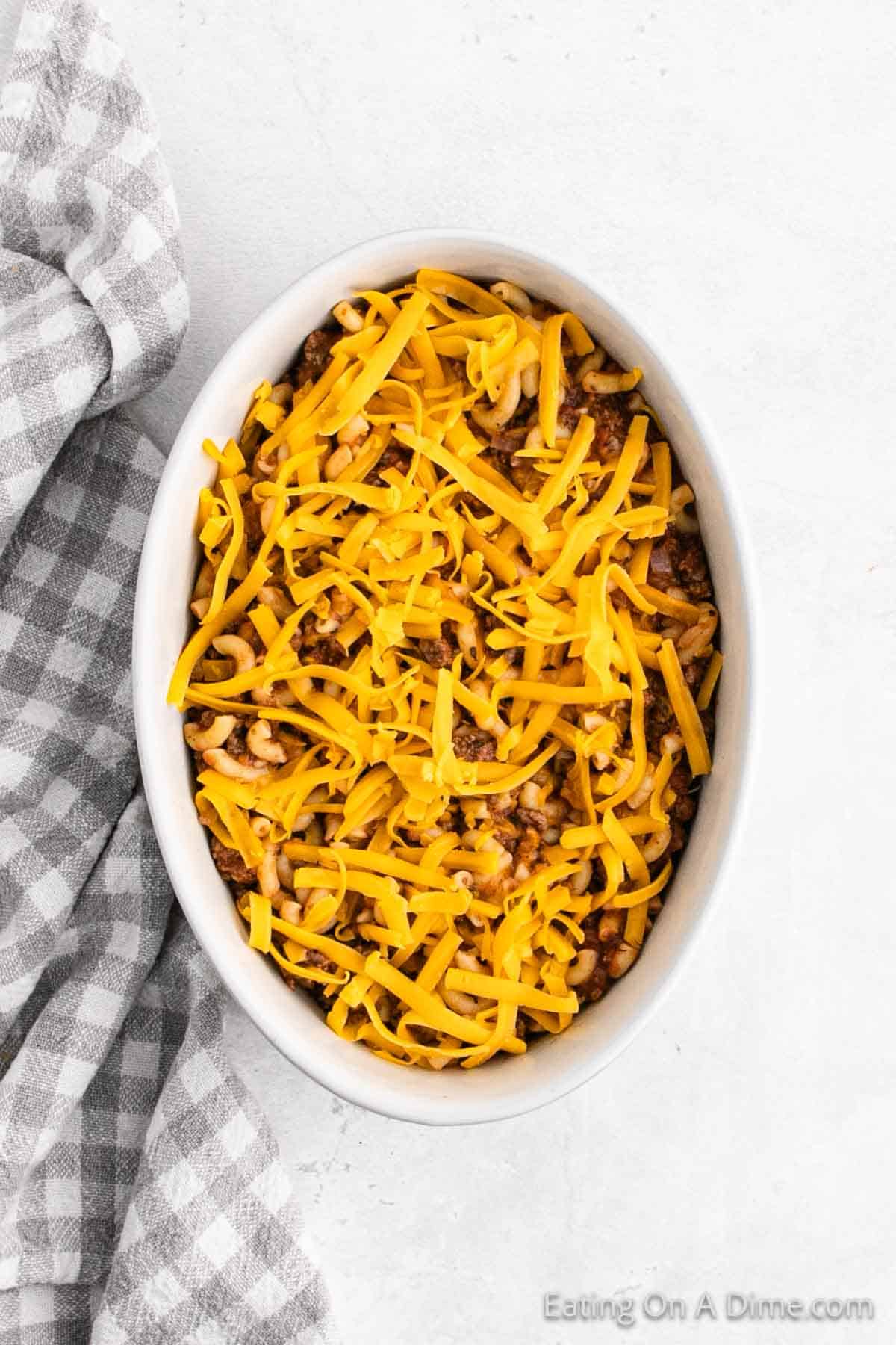 Pouring the meat mixture in a casserole dish topped with shredded cheese