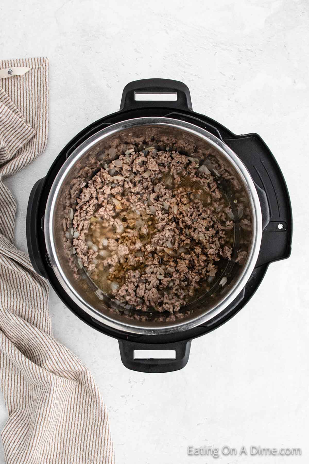 A cooking pot containing freshly cooked ground meat is placed on a light-colored surface. A striped cloth lies next to the pot. The meat, perfect for making an instant pot southwest egg roll in a bowl, is slightly browned and ready for further preparation.