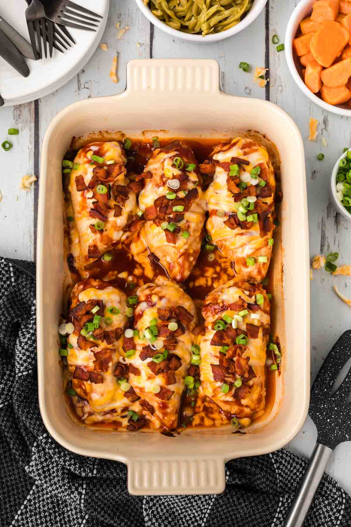 BBQ Baked Chicken in a baking dish topped with chopped bacon and green onions and melted cheese