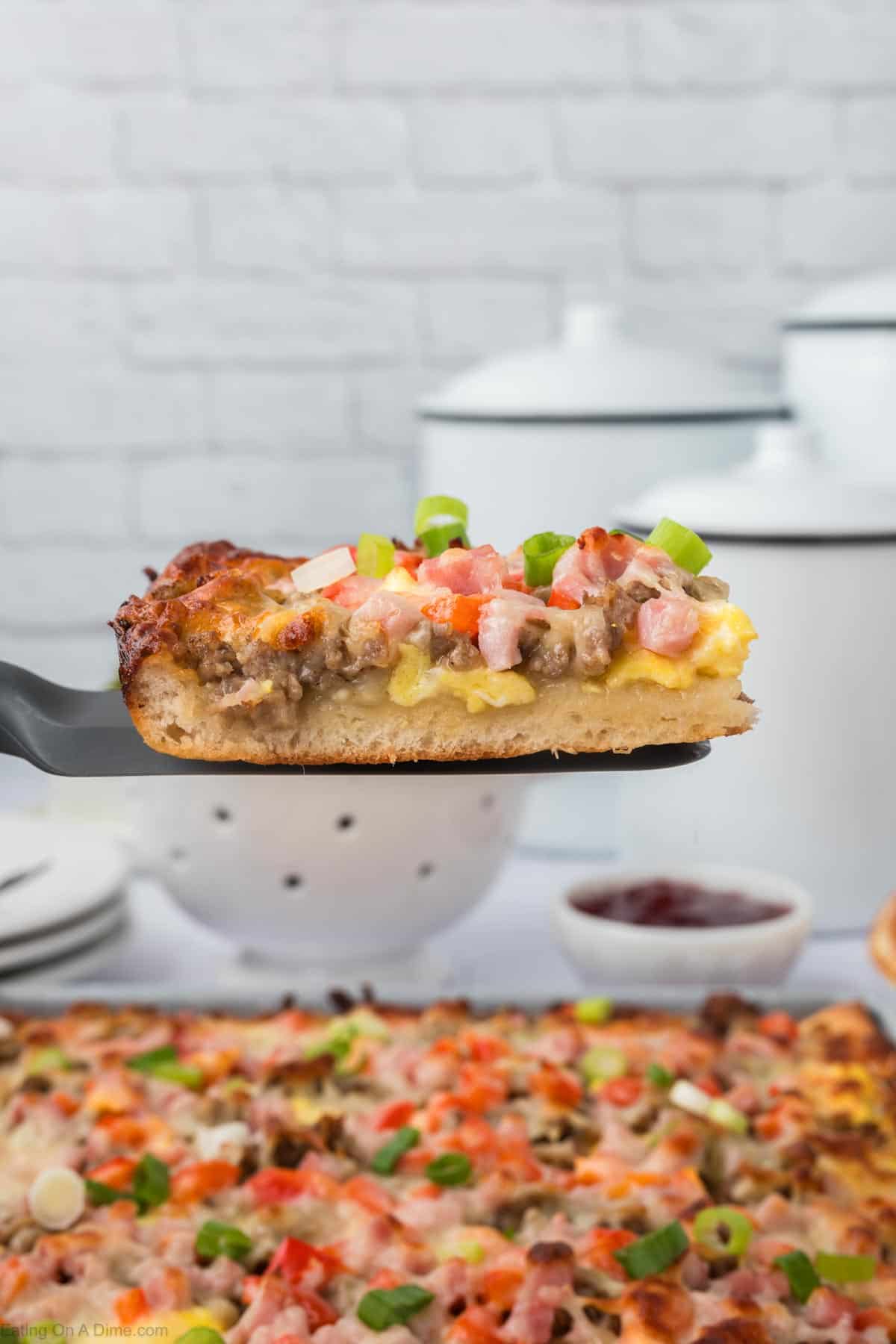 Slice of breakfast pizza on a spatula with breakfast pizza in the background