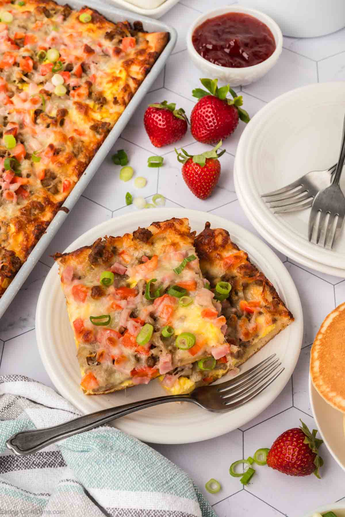 Breakfast Pizza Stacked on a plate with a pan of breakfast pizza and fresh strawberries on the side