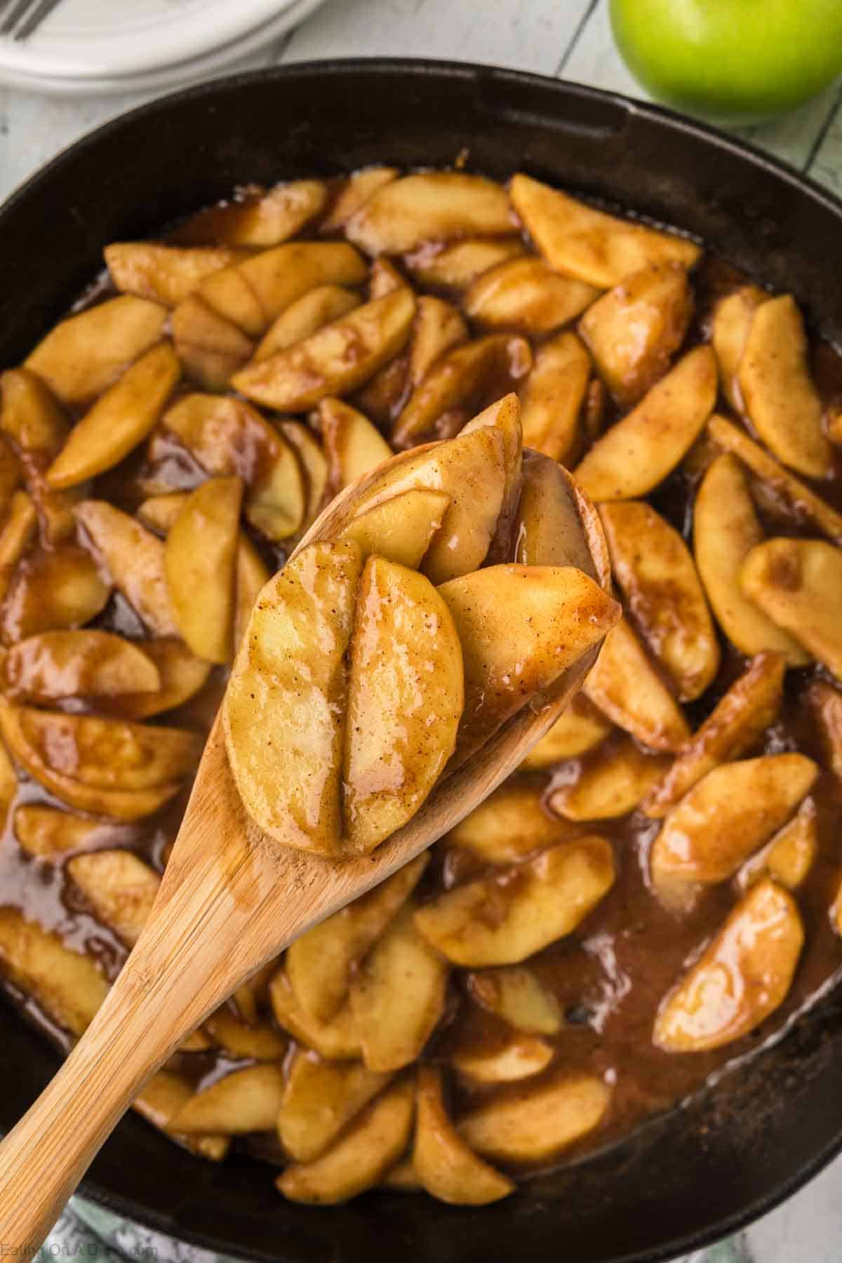 Fried slice apples in a cast iron skillet with a serving on a wooden spoon