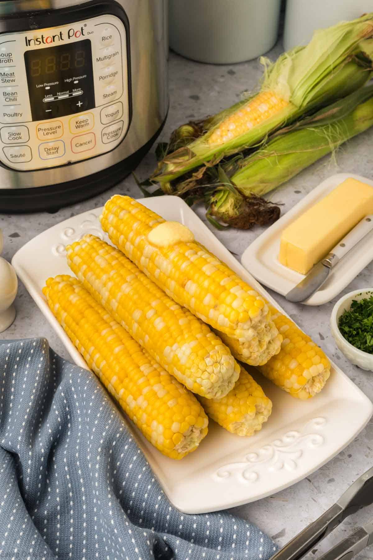 Corn on the cob stacked on a white platter topped with butter 