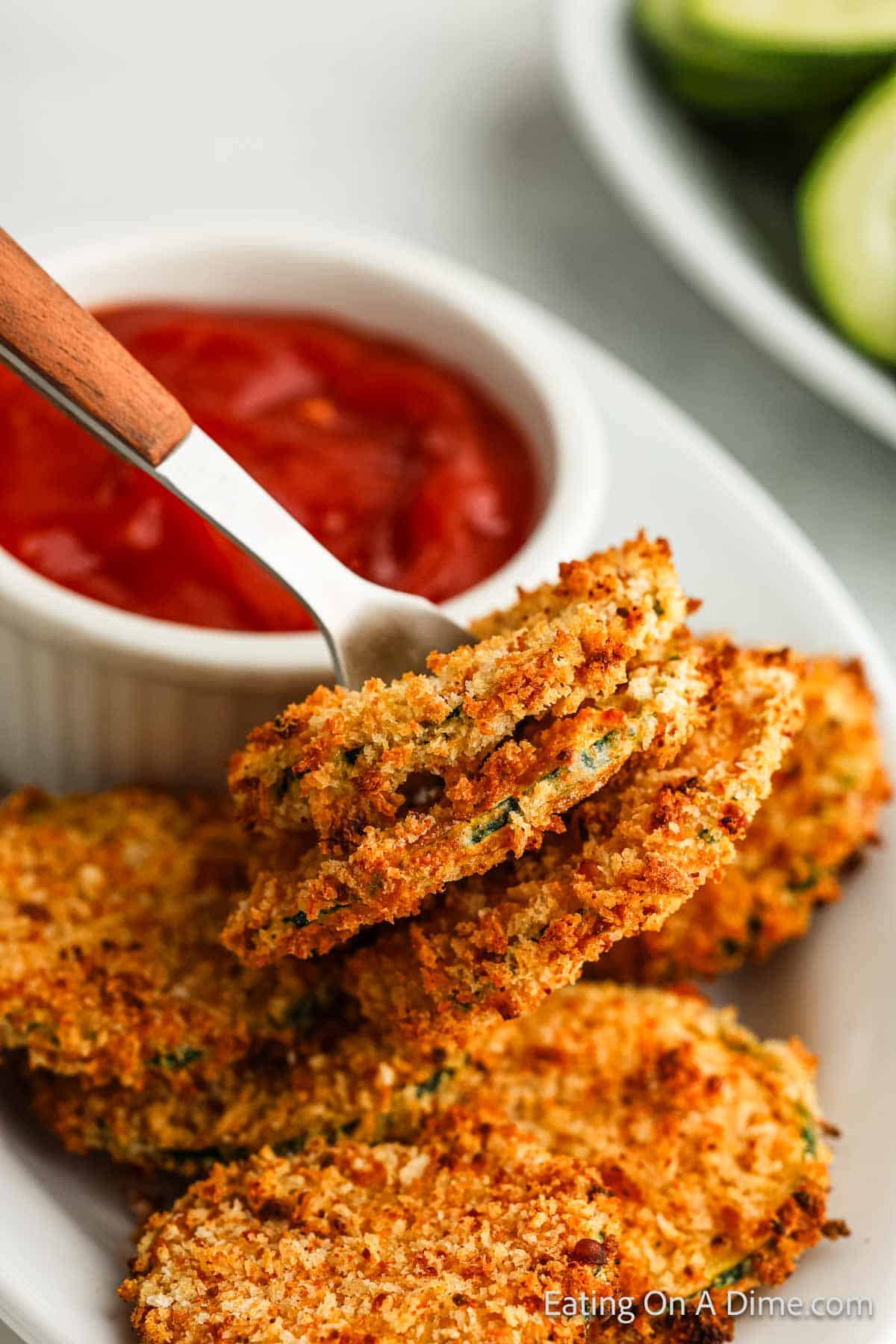 Zucchini chips on a plate with a side of ketchup in a bowl with a serving on a fork