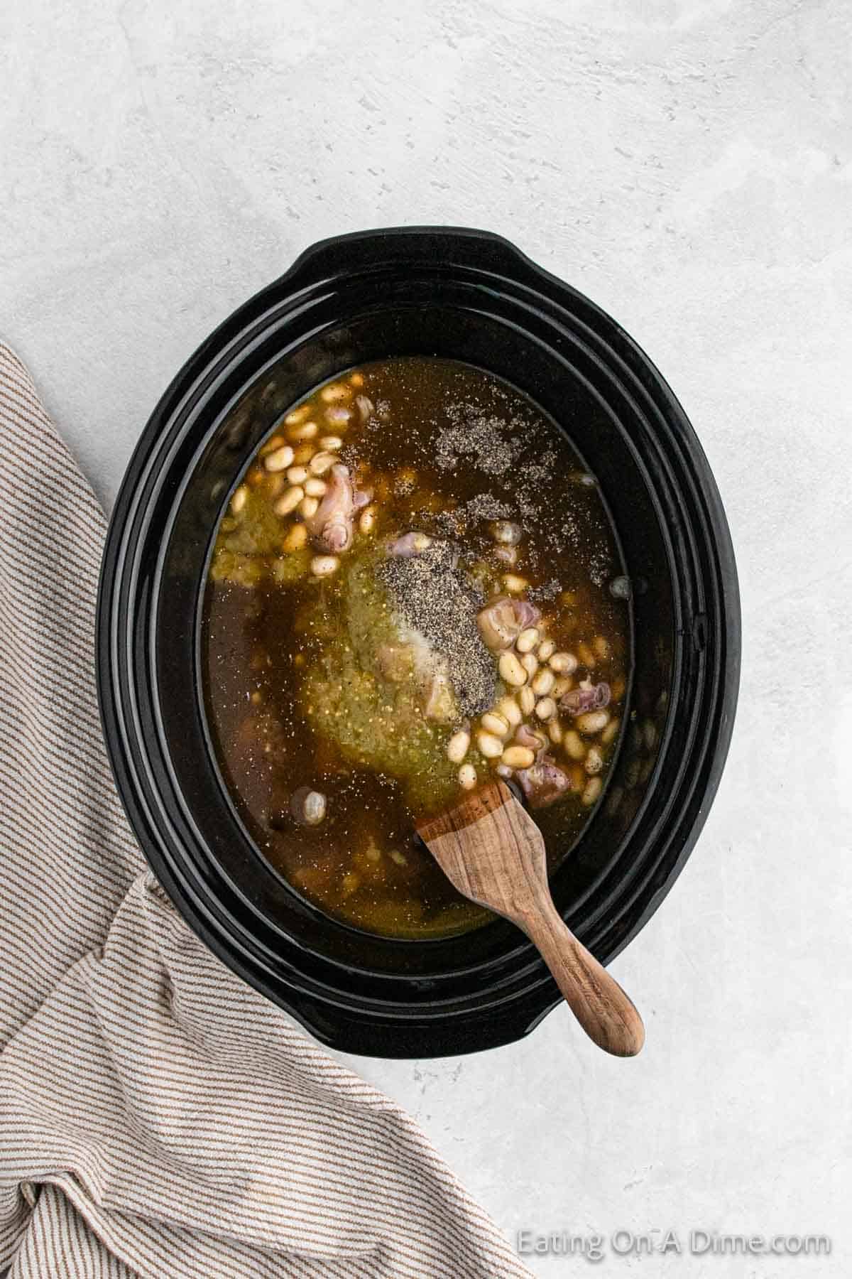 Placing chicken with the beans and sauce in the slow cooker