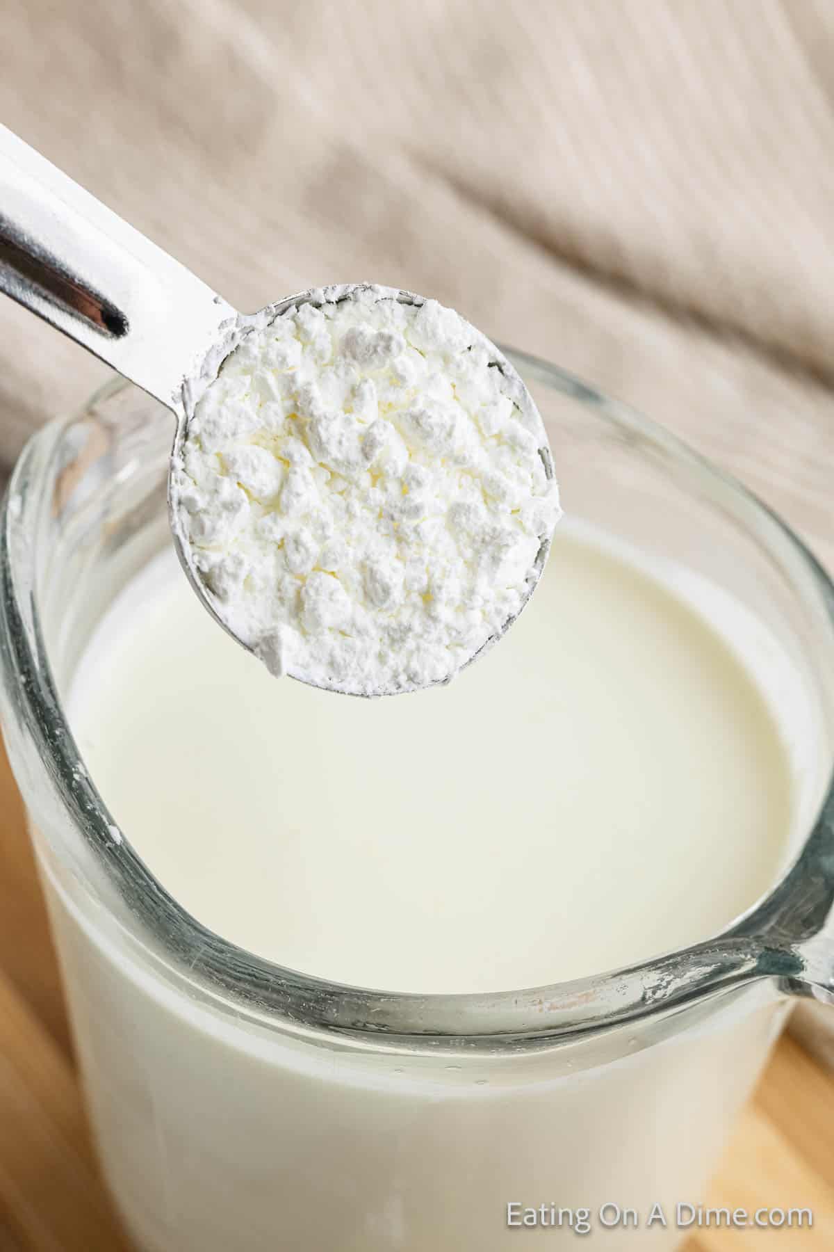 Cornstarch in a measuring cup over a cup of heavy whipping cream