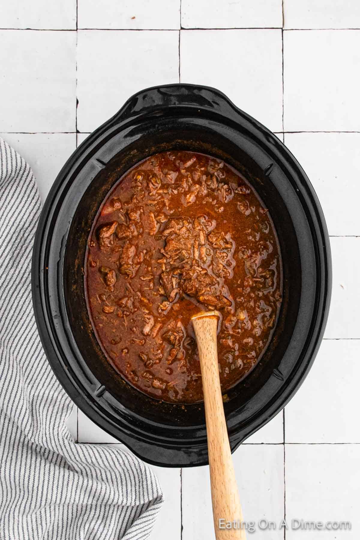 Cooked beef mixture in the slow cooker with a wooden spoon