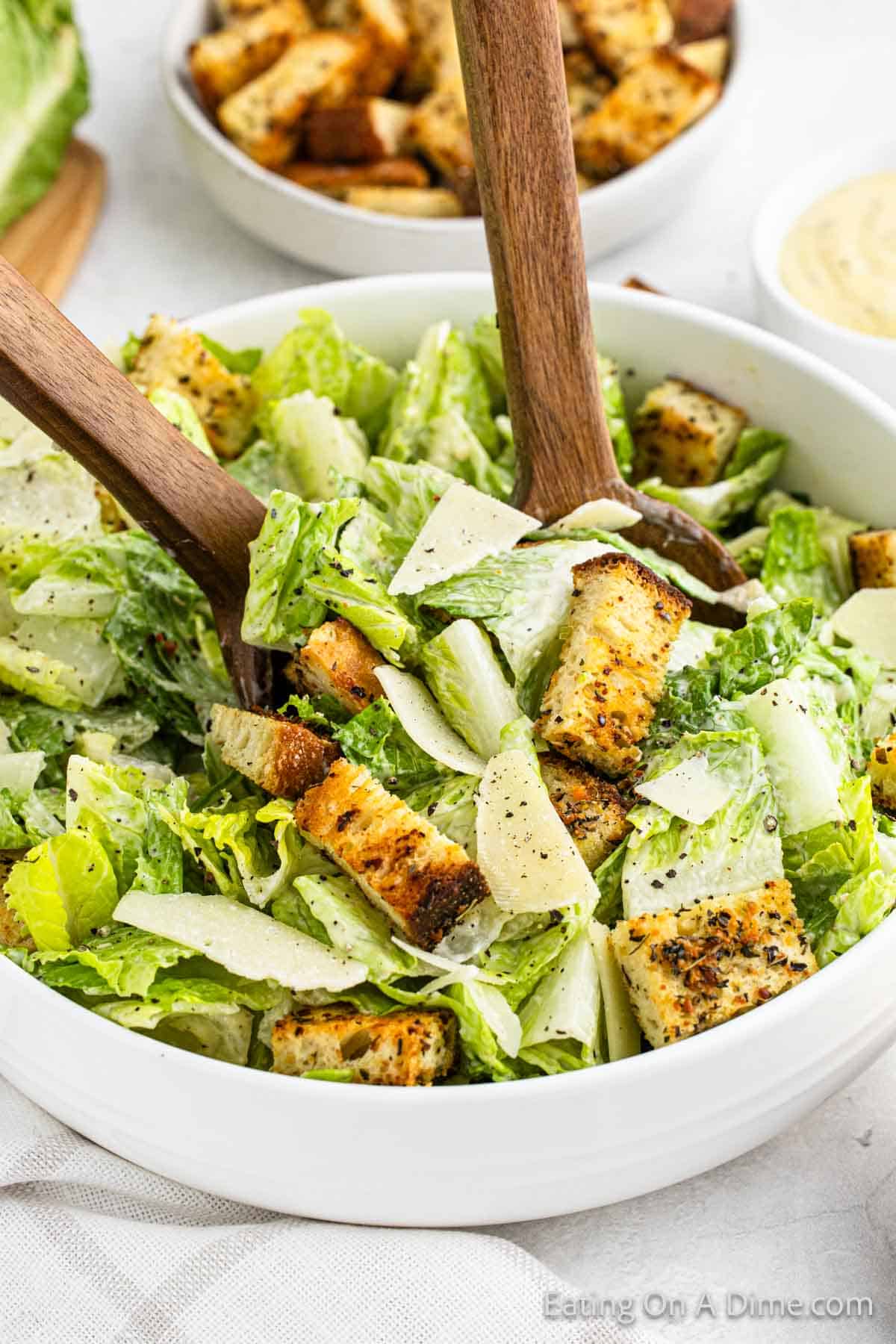 Caesar Salad in a bowl topped with croutons with wooden spoons