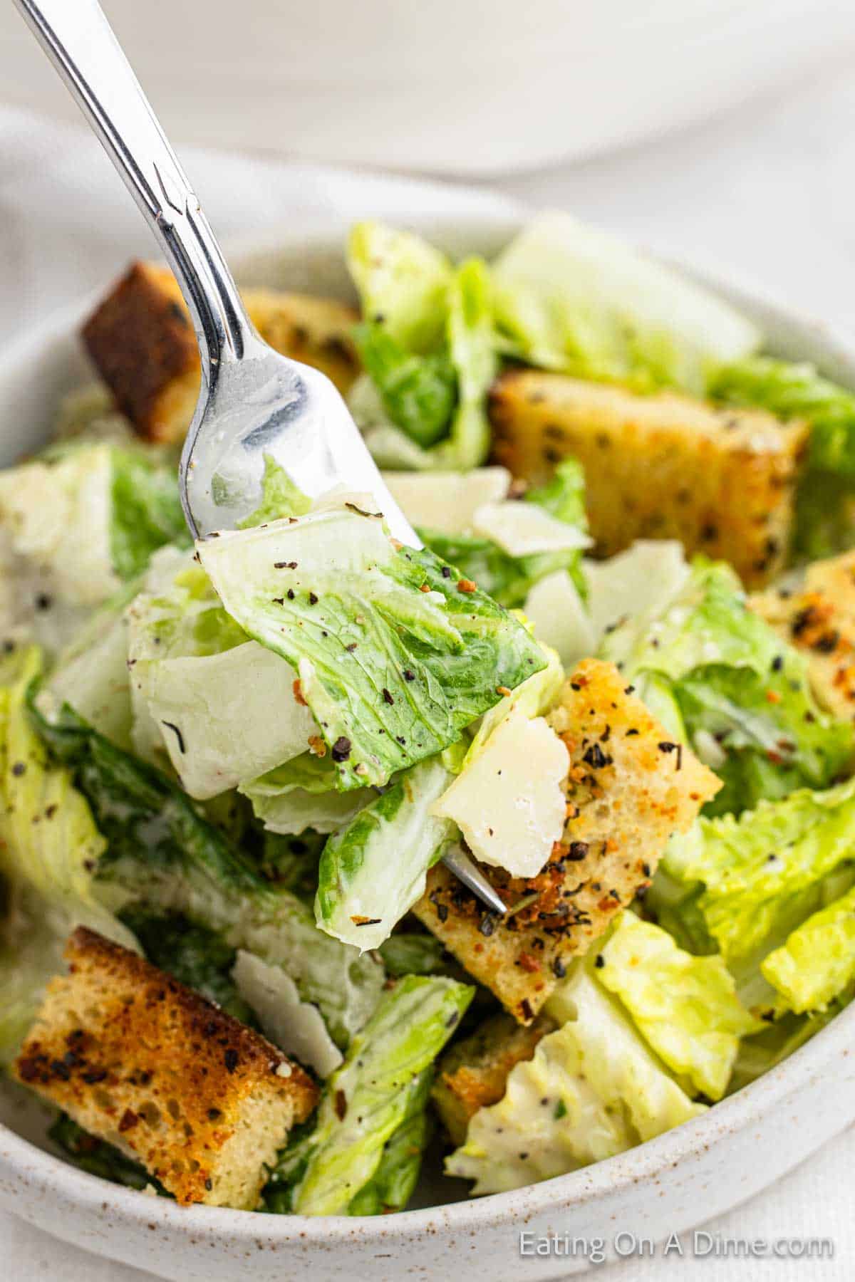 Caesar Salad in a bowl topped with croutons with a bite on a fork