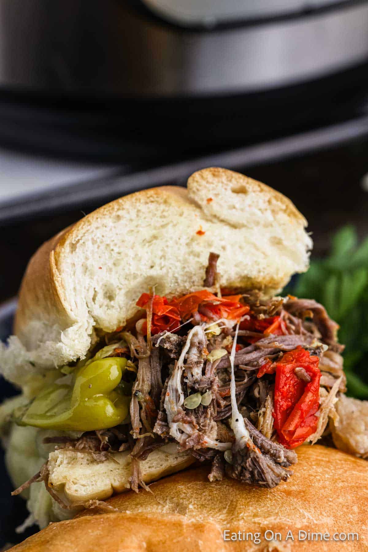 Italian Beef Sandwich cut in half with shredded beef topped with melted cheese and peppers