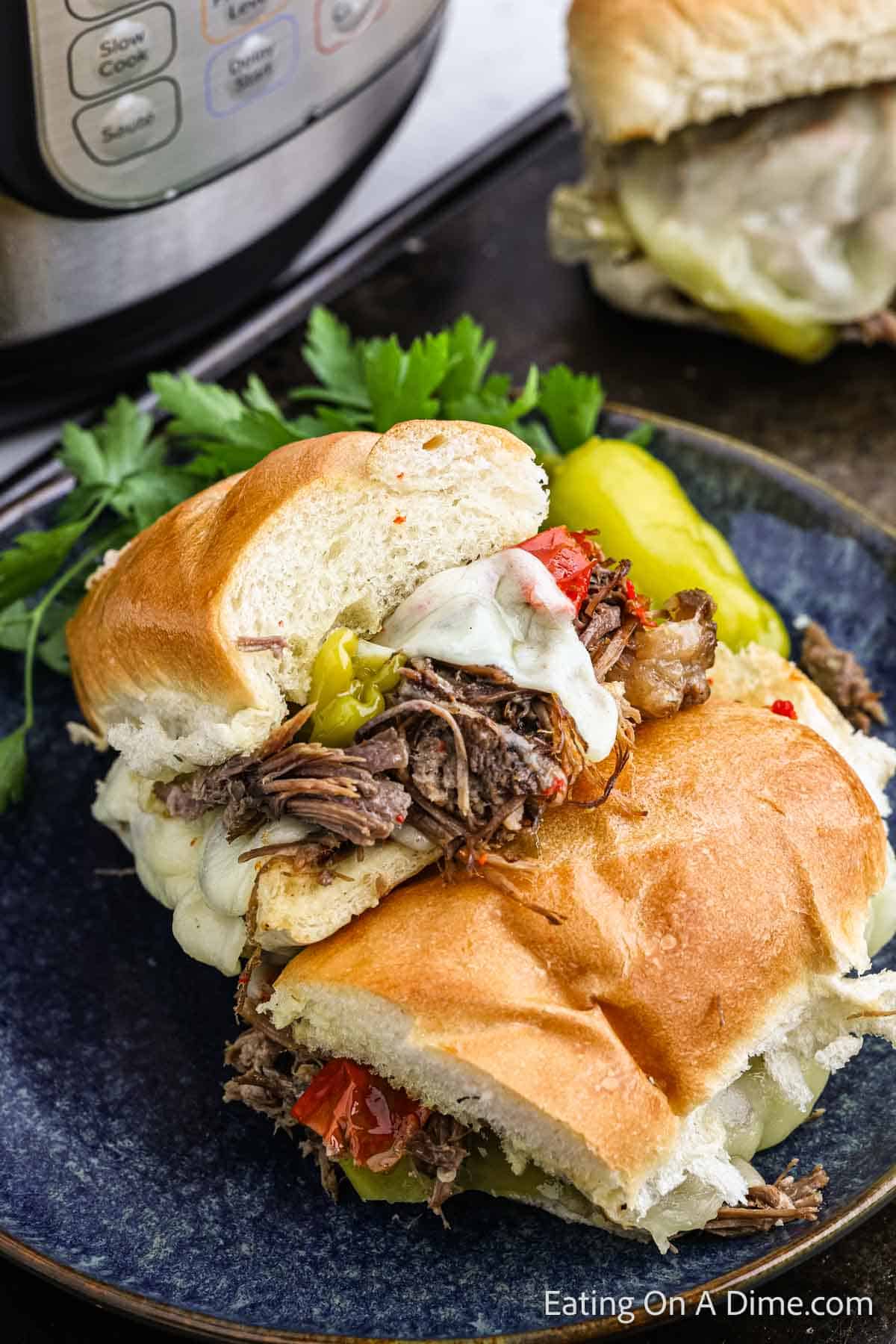 Italian Beef Sandwich cut in half with shredded beef topped with melted cheese and peppers on a plate