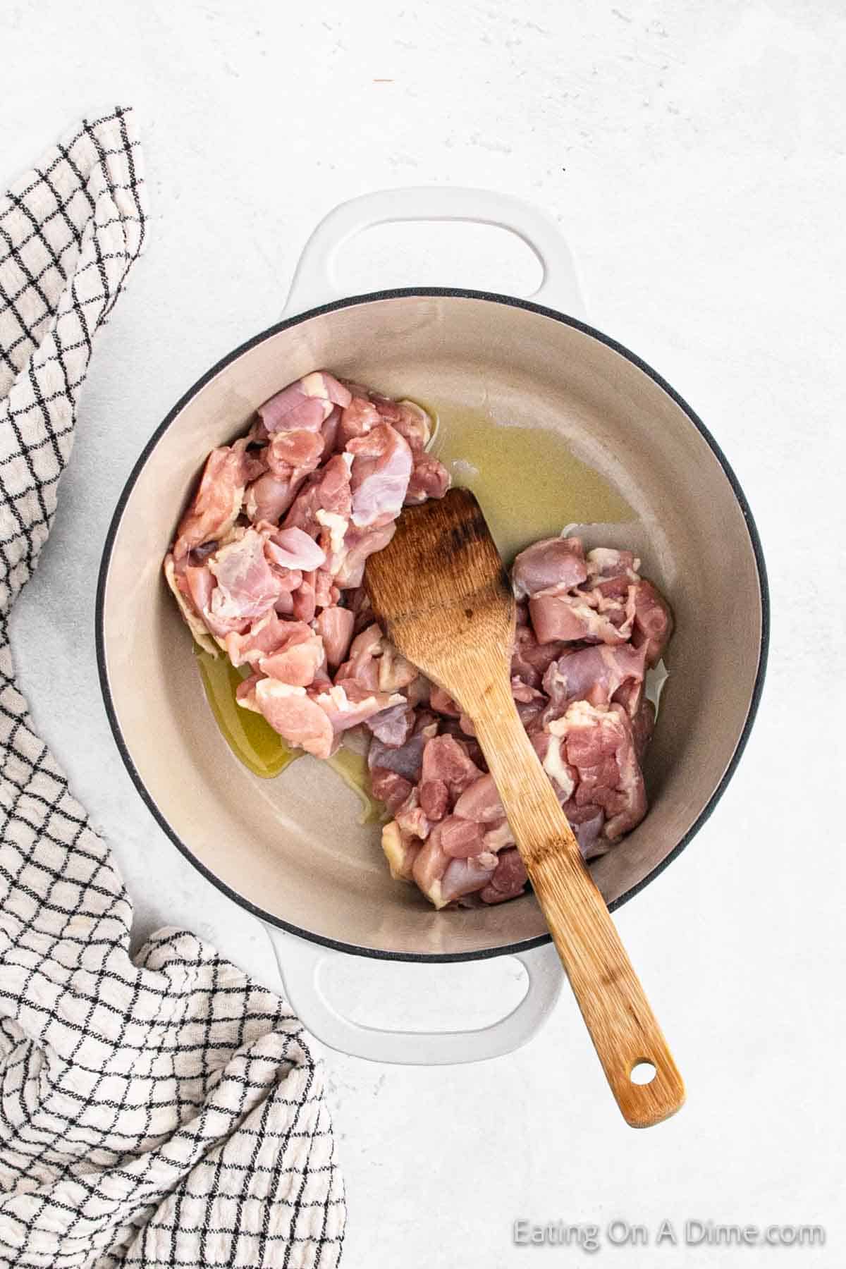 Cooking diced chicken thighs in a large pot with a wooden spoon