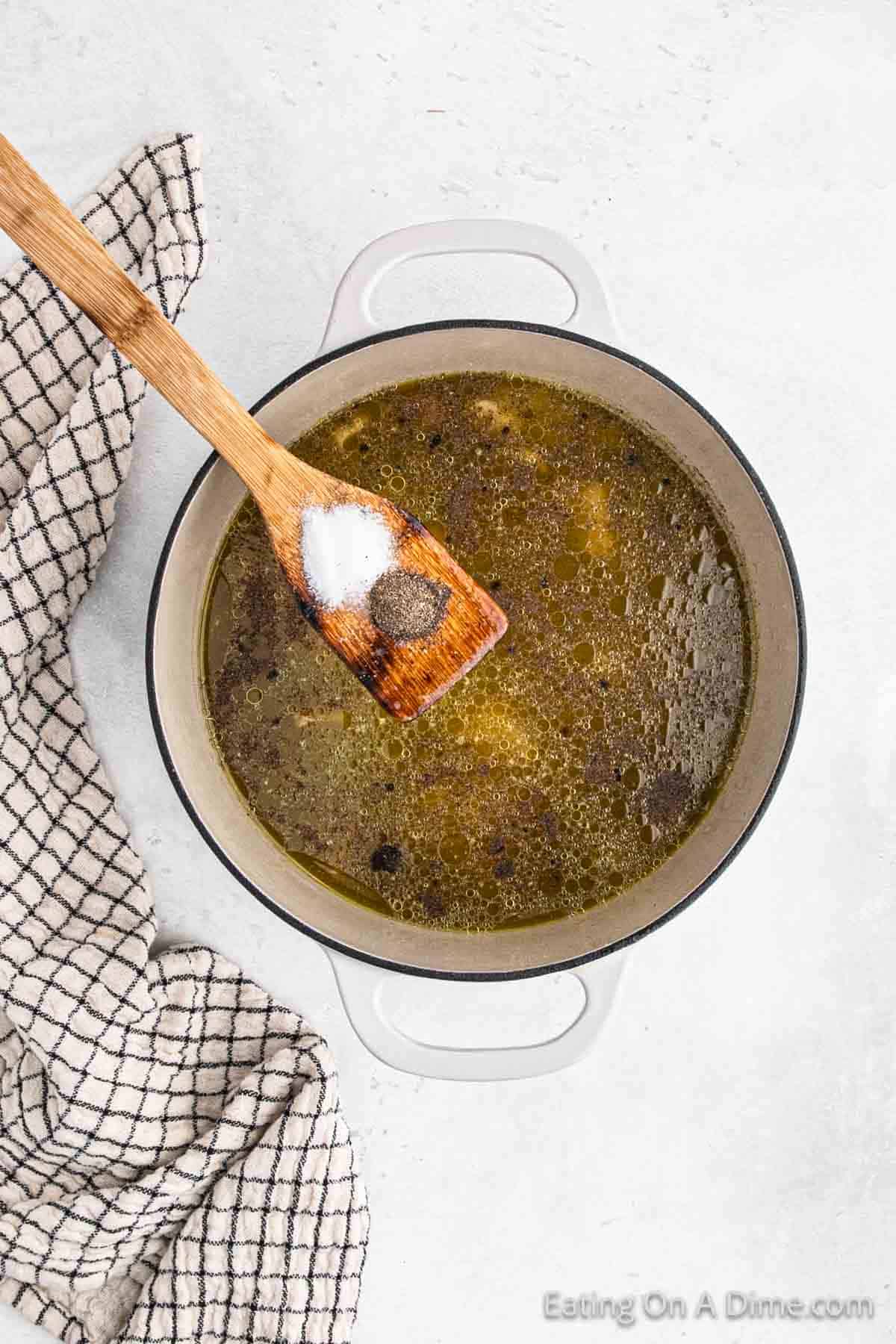 Mixing together enchilada sauce, salsa verde, chicken broth, salt and pepper in a large pot with a wooden spoon