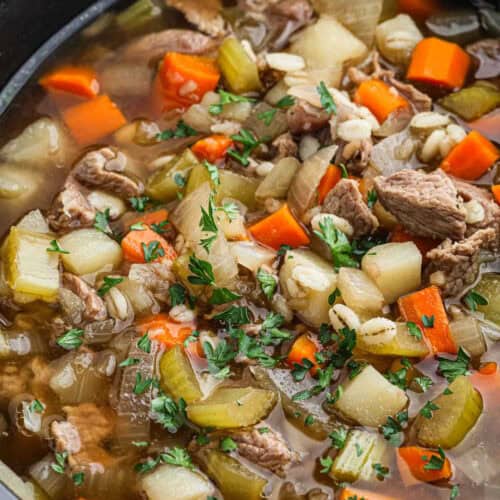 A close-up of a hearty crockpot beef barley soup in a bowl, featuring chunks of tender beef, diced carrots, celery, and onions, with barley grains. The soup is garnished with fresh parsley, creating a warm and comforting dish.