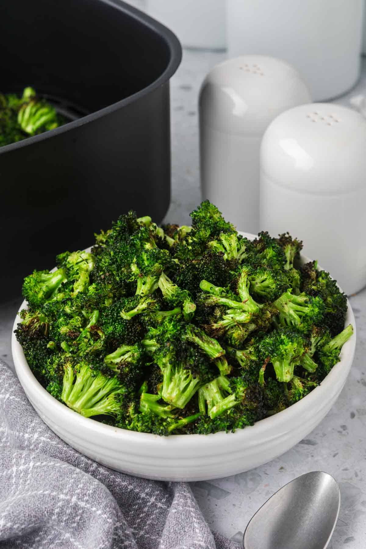 A white bowl of air fryer broccoli with an air fryer in the back ground