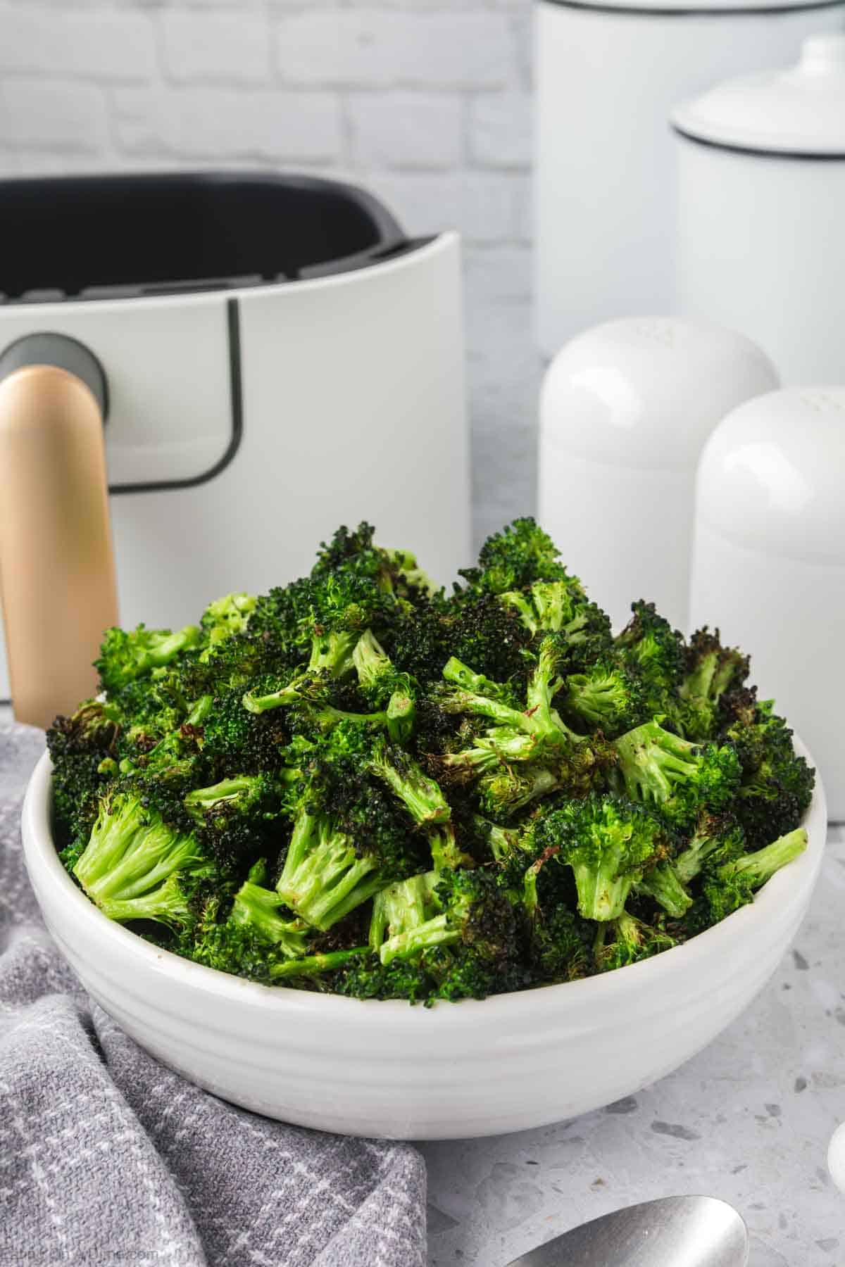A white bowl full of air fryer broccoli with an air fryer in the background
