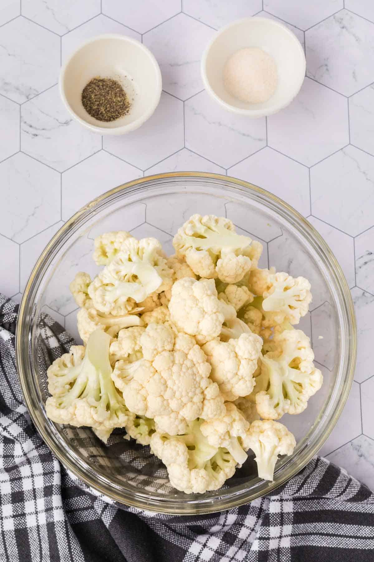 Ingredients - Cauliflower cut into chunks with small bowls of garlic salt and pepper on the side