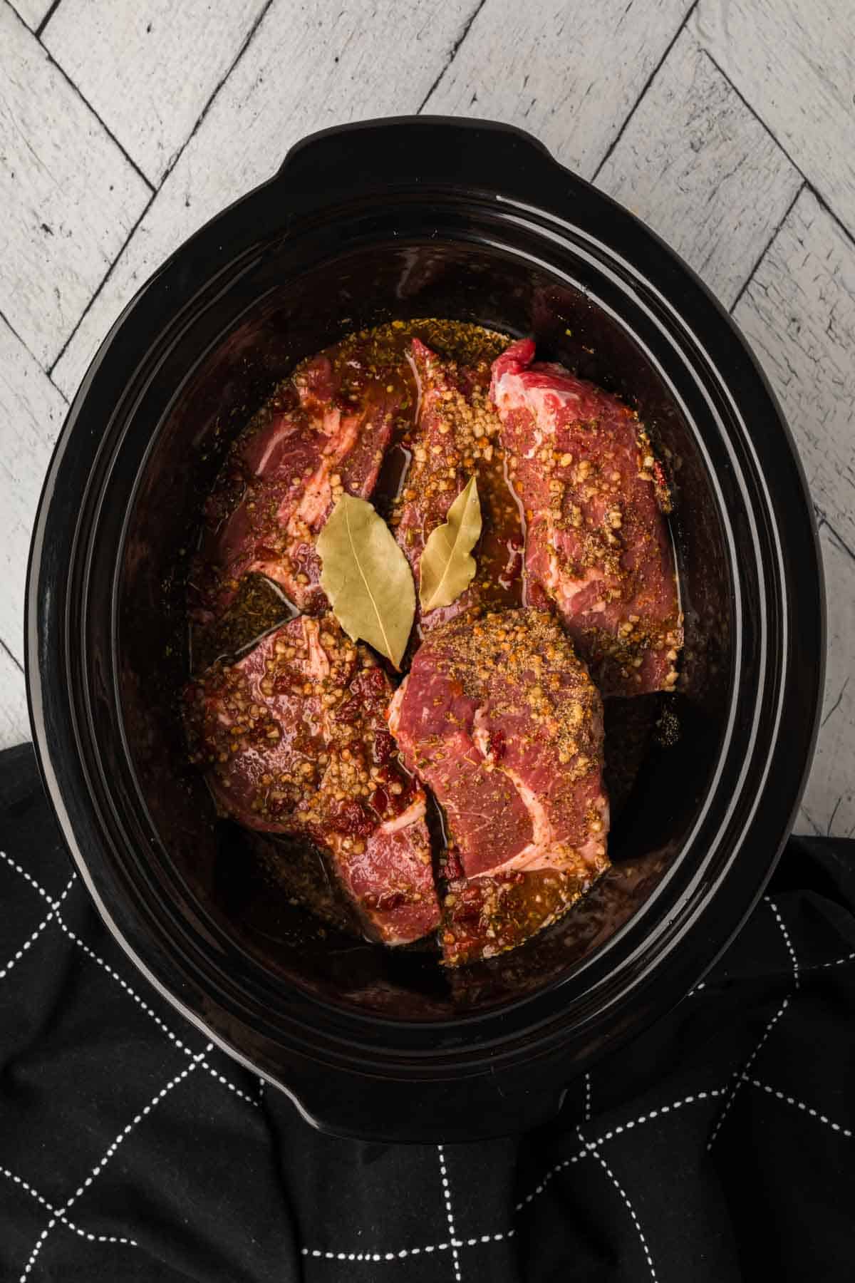 Topping the large beef roast pieces topped with seasoning in the slow cooker