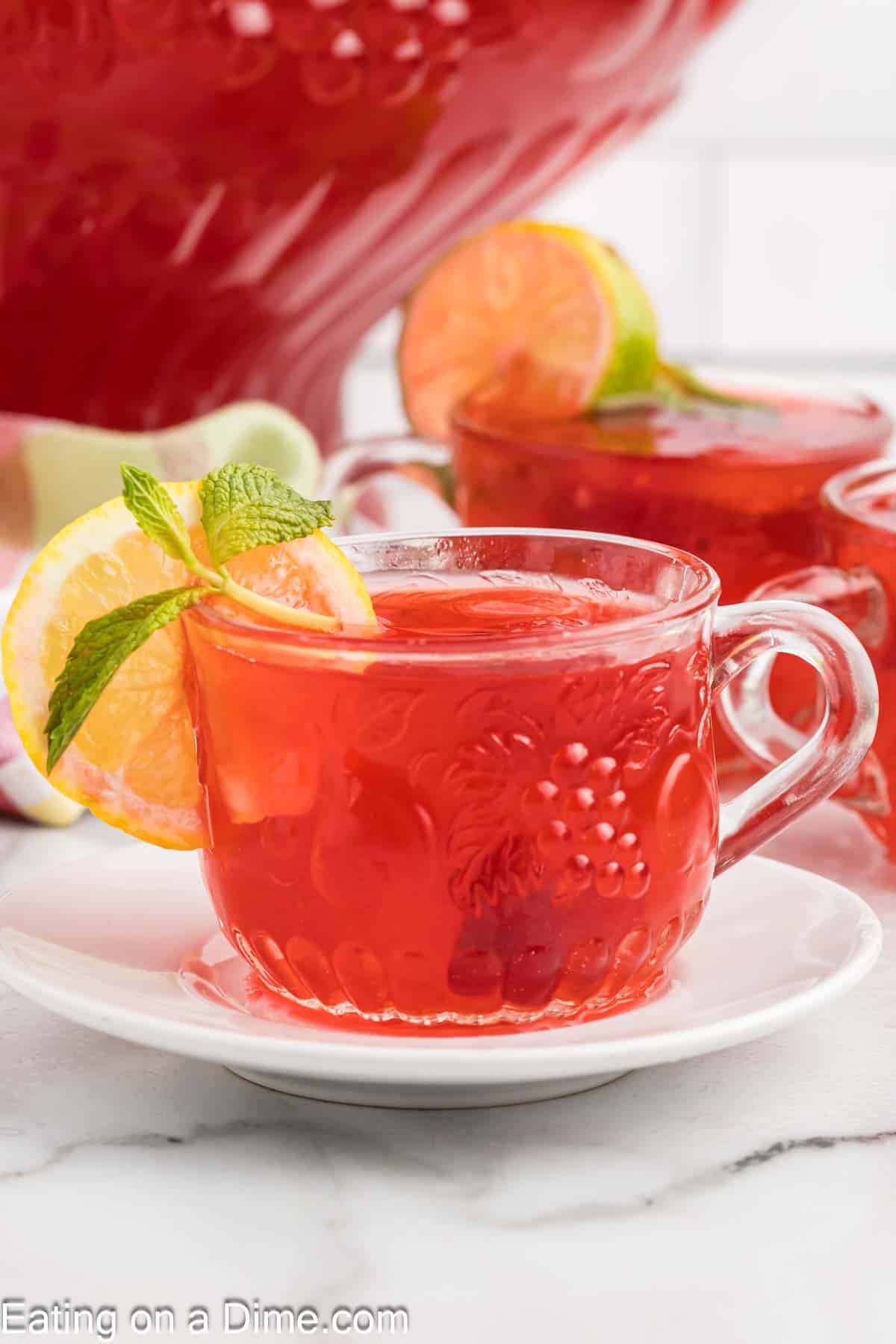 A clear glass mug with punch and garnished with lemon slices and mint