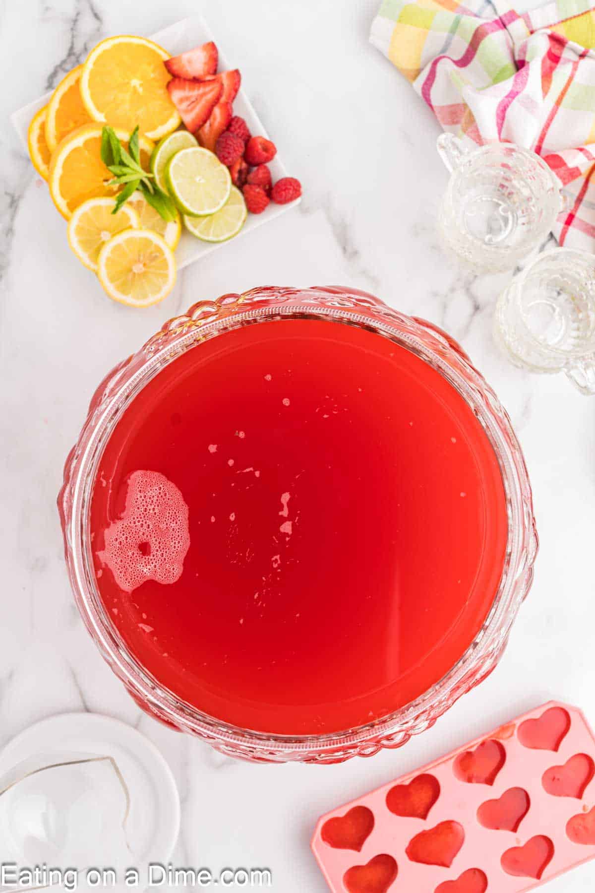 Party punch in a large clear bowl with a plate of lemon slices, orange slices, lime slices and strawberries