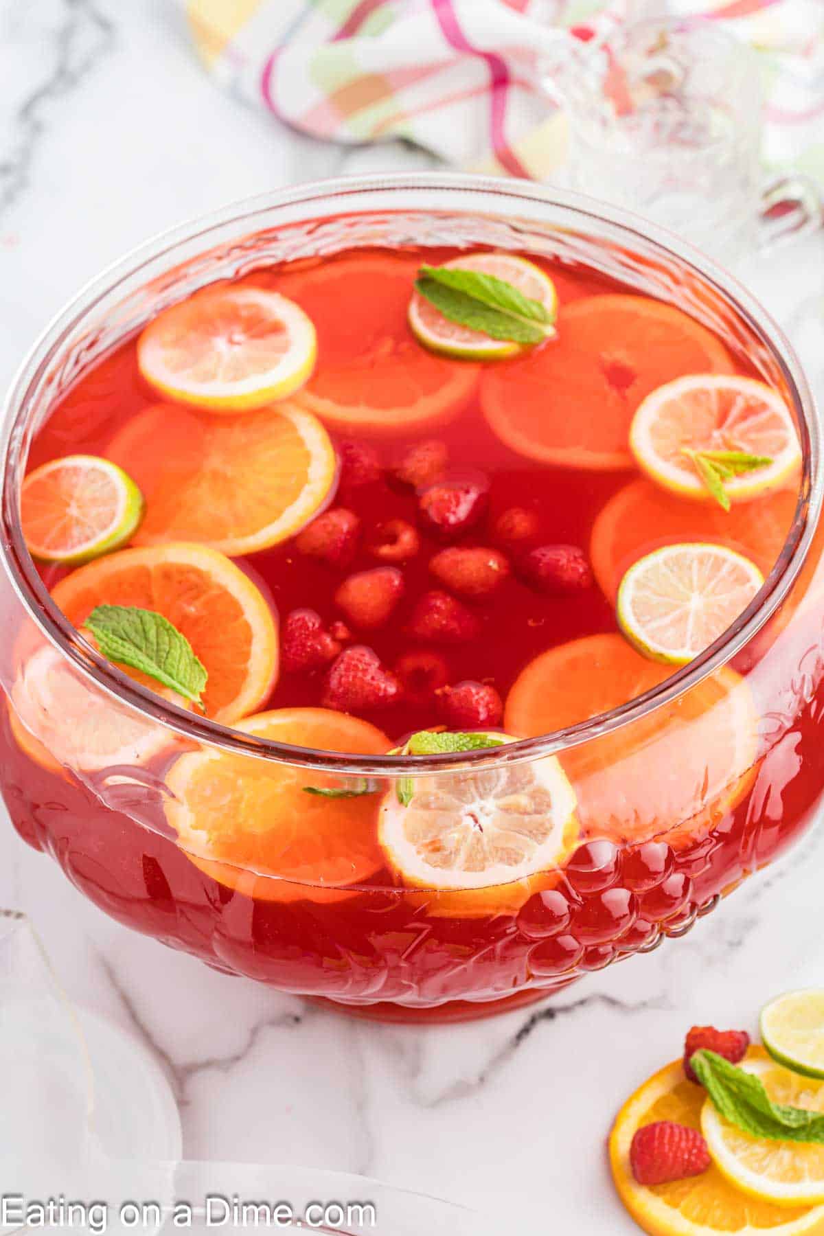 Party punch in a large clear bowl with lemon, orange and lime slices with strawberries and fresh mint floating in it