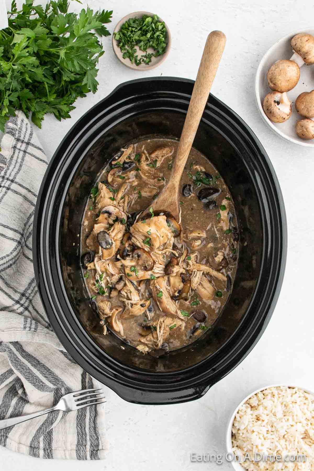 Cream of mushroom chicken in a slow cooker with a wooden spoon