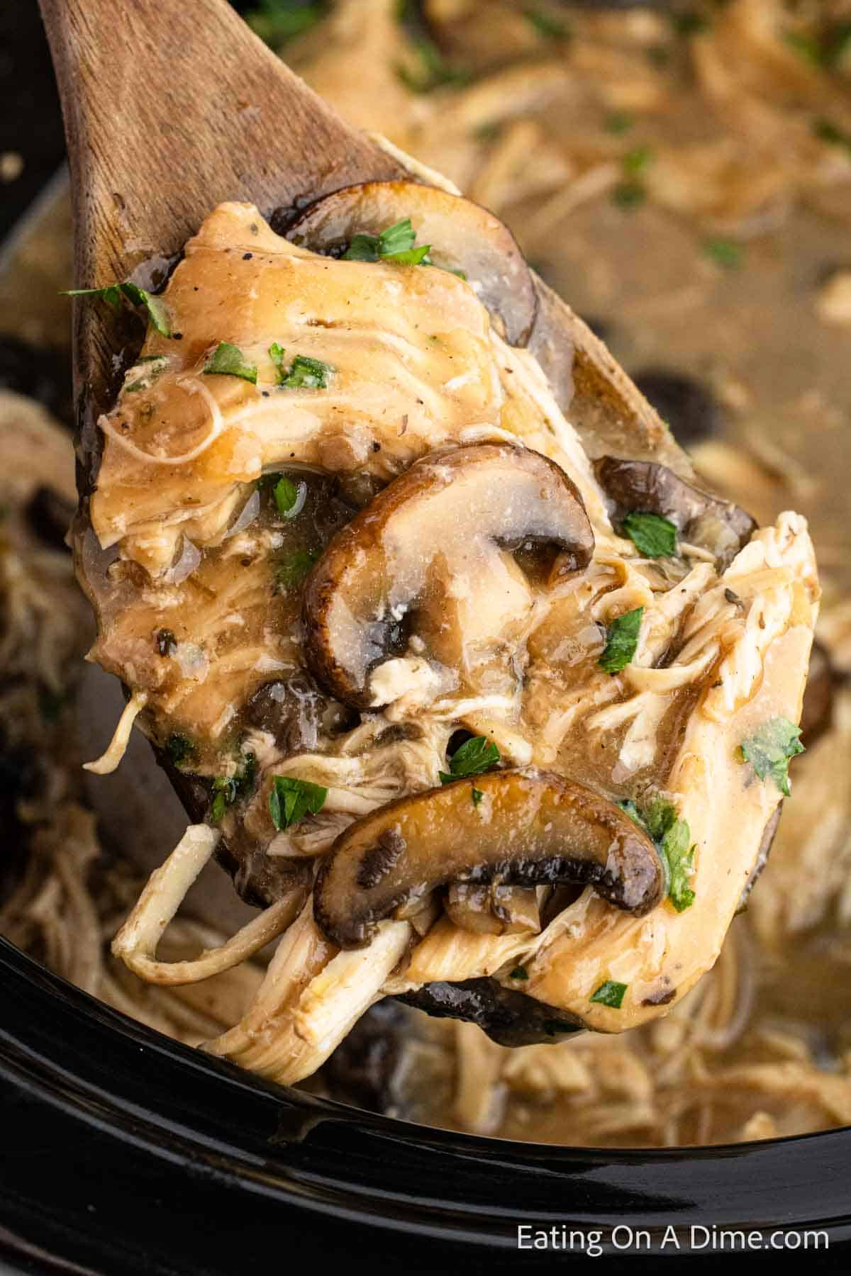 Shredded chicken in sauce with mushrooms on a wooden spoon