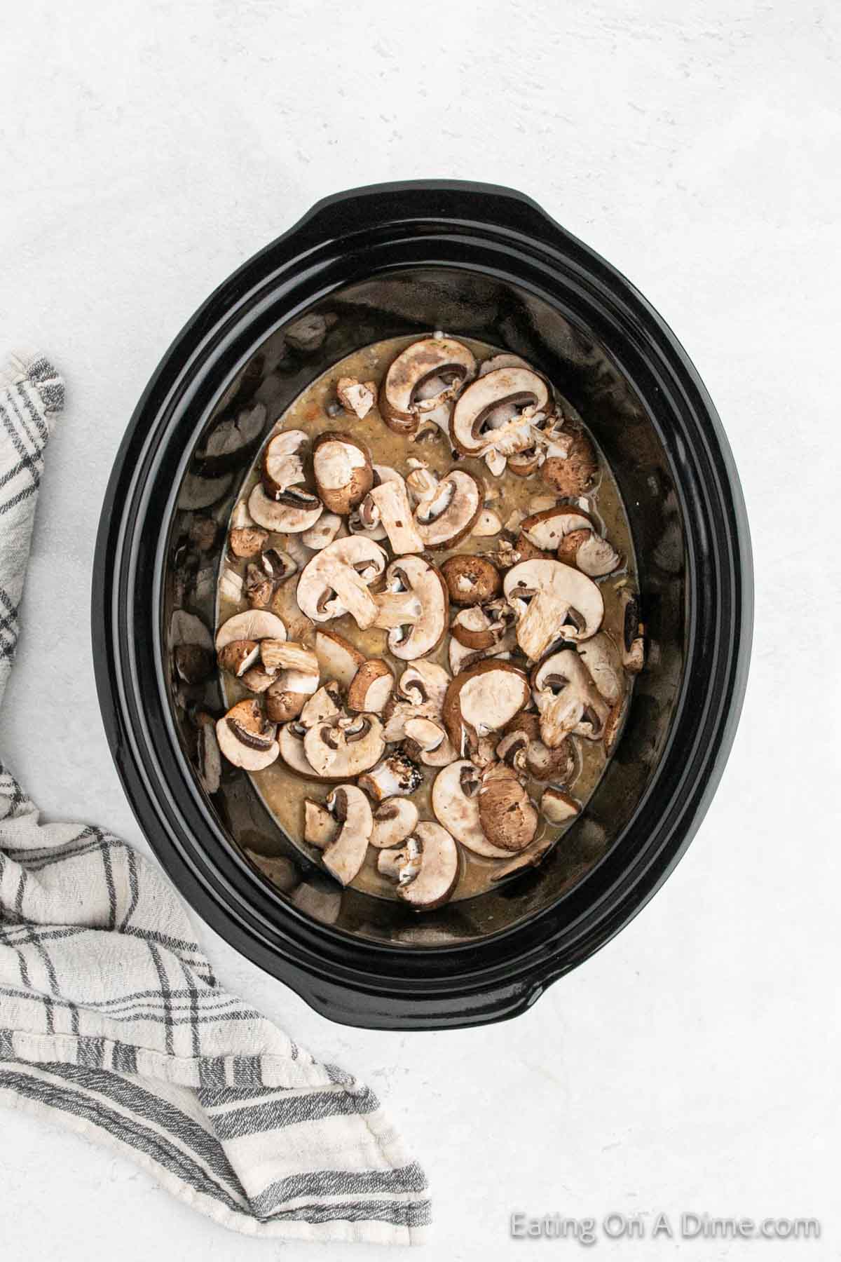 Topping slice mushrooms over the chicken and sauce mixture in the slow cooker