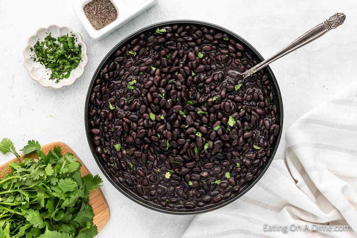 Cooked black beans in a bowl with a side of fresh cilantro