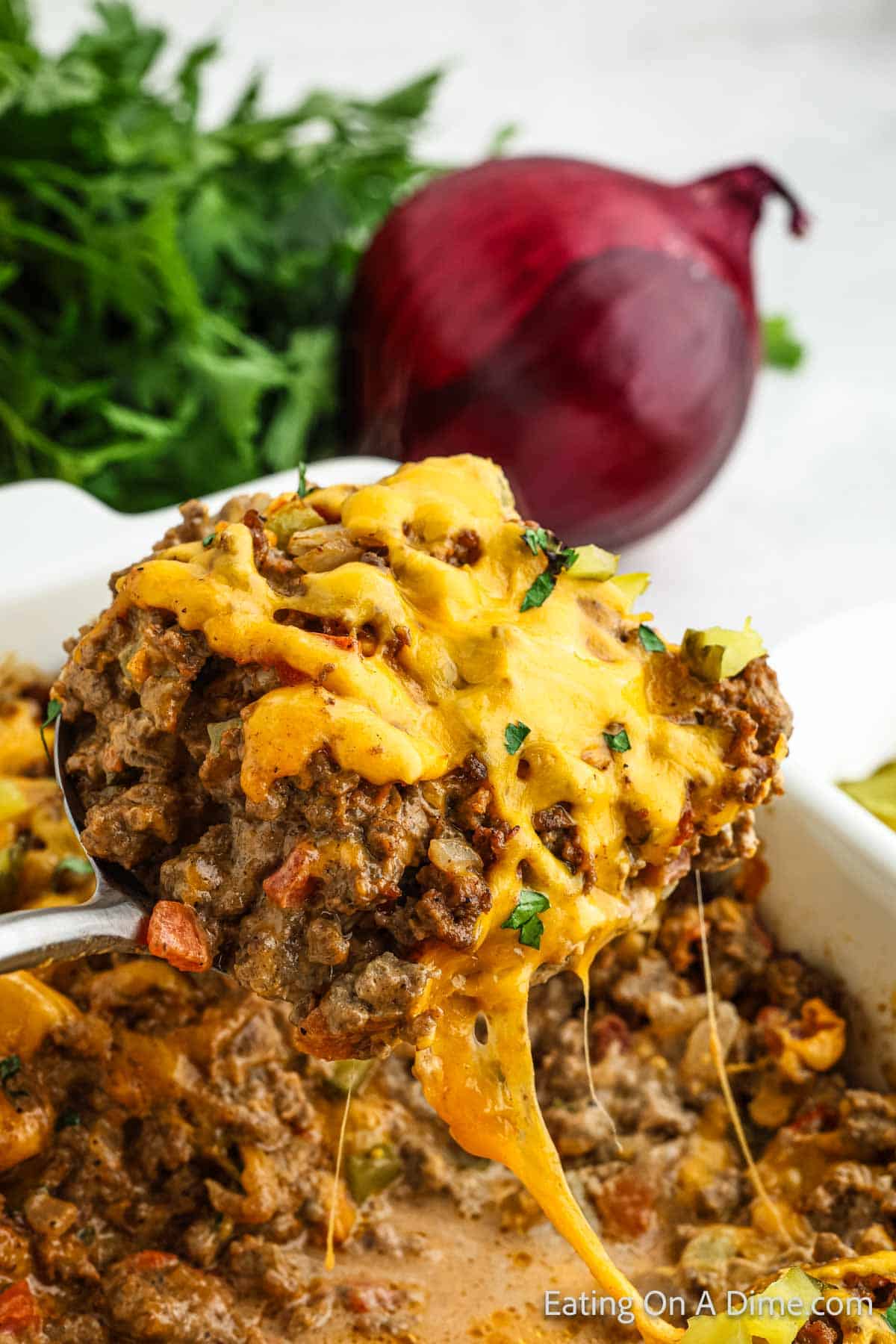 Cheeseburger Casserole topped with melted cheese in a casserole dish with a serving on a silver spoon