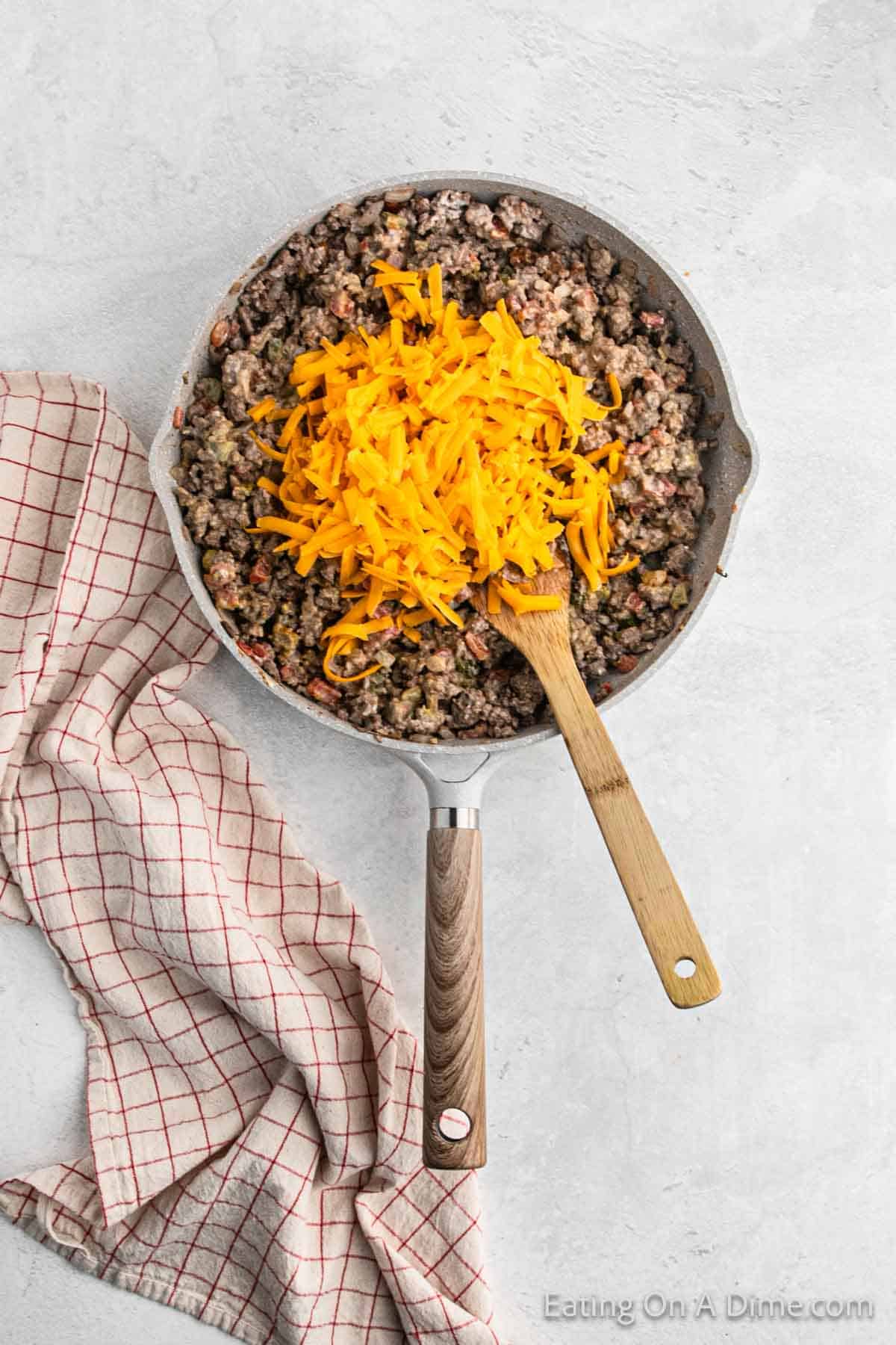 Ground beef mixture in a skillet topped with shredded cheese with a wooden spoon