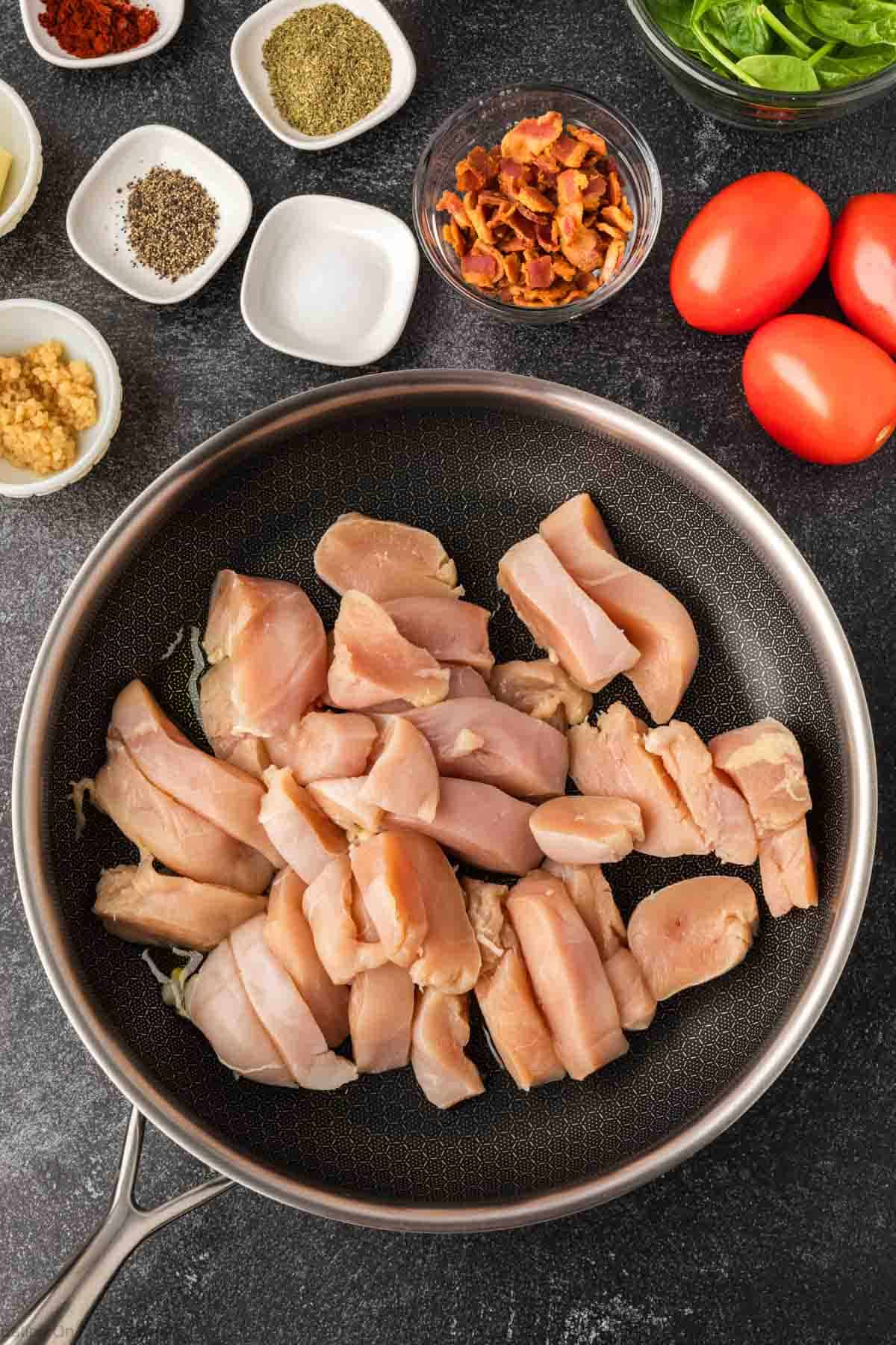 Cooking chicken in a skillet with small bowls of seasoning on the side