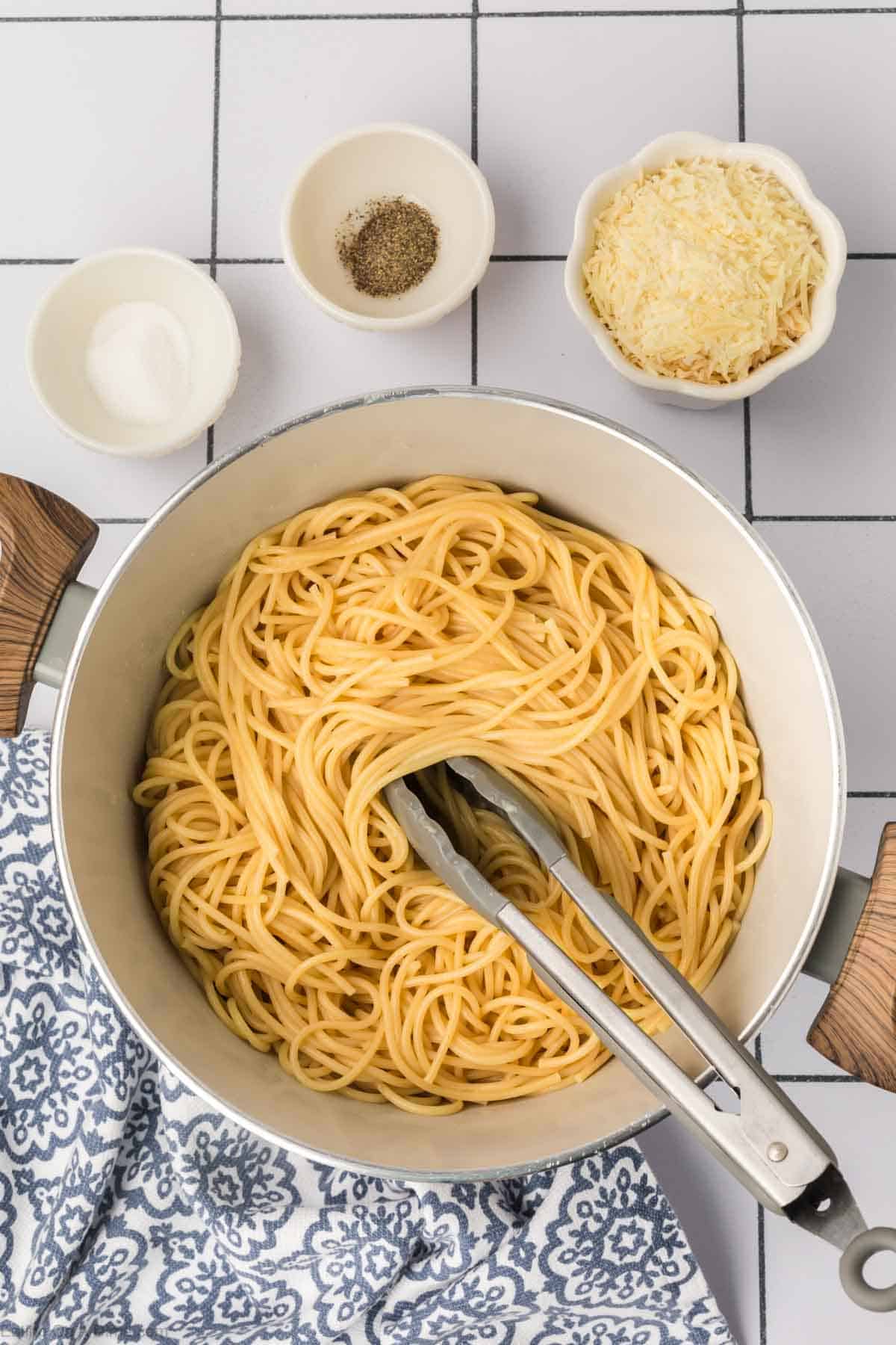 Tossing the pasta in a large pot with tongs