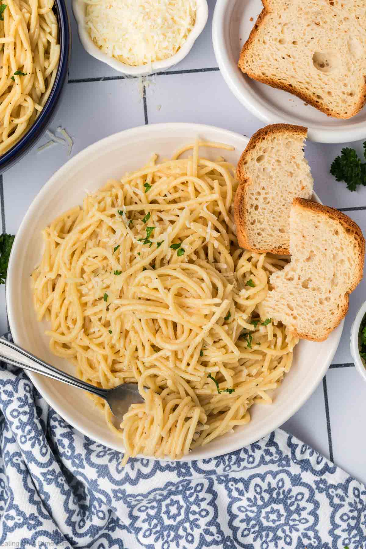 Spaghetti mixed in a creamy sauce on a plate with a side of bread