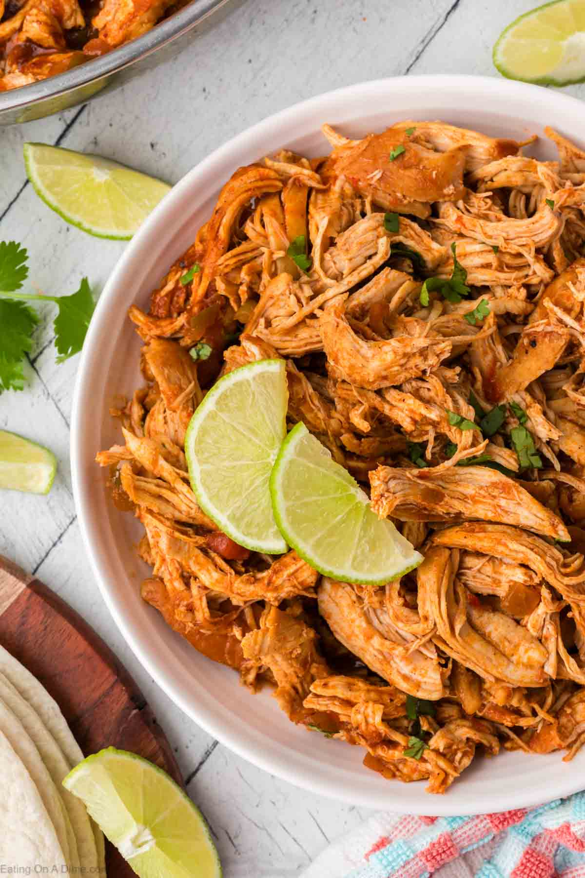 Shredded Mexican Chicken in a bowl topped with fresh cilantro and fresh lime wedges