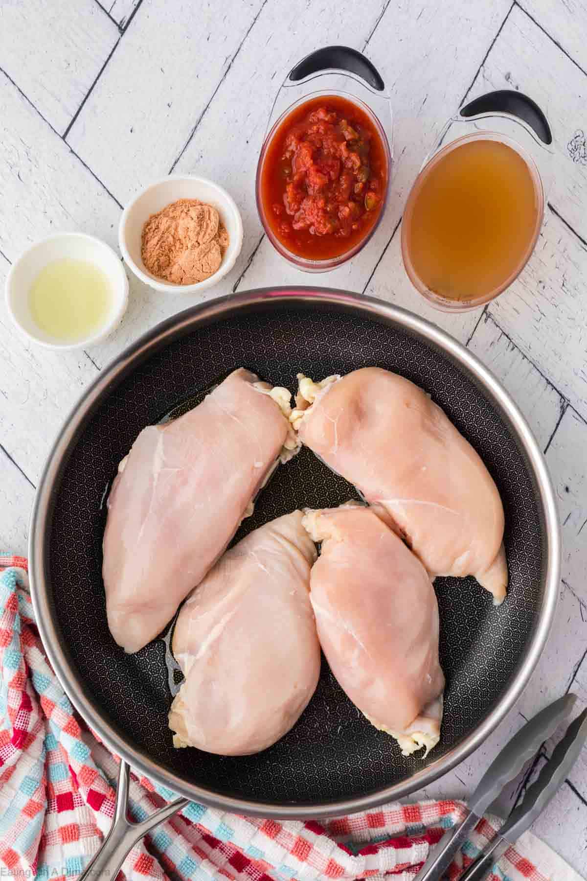 Chicken Breast in the skillet with small bowls of oil, taco seasoning, broth and salsa on the side