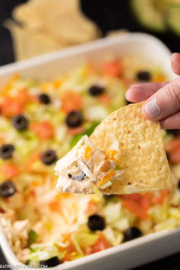 Close up image of Taco Dip in a white dish with a serving on a chip. 