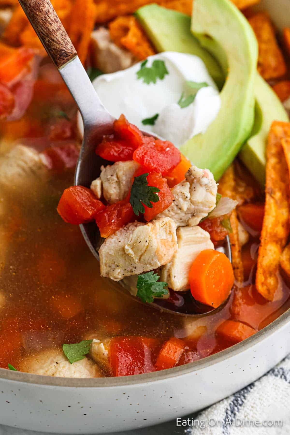 Mexican Chicken Soup in a bowl topped with avocado and sour cream with a bite on a spoon