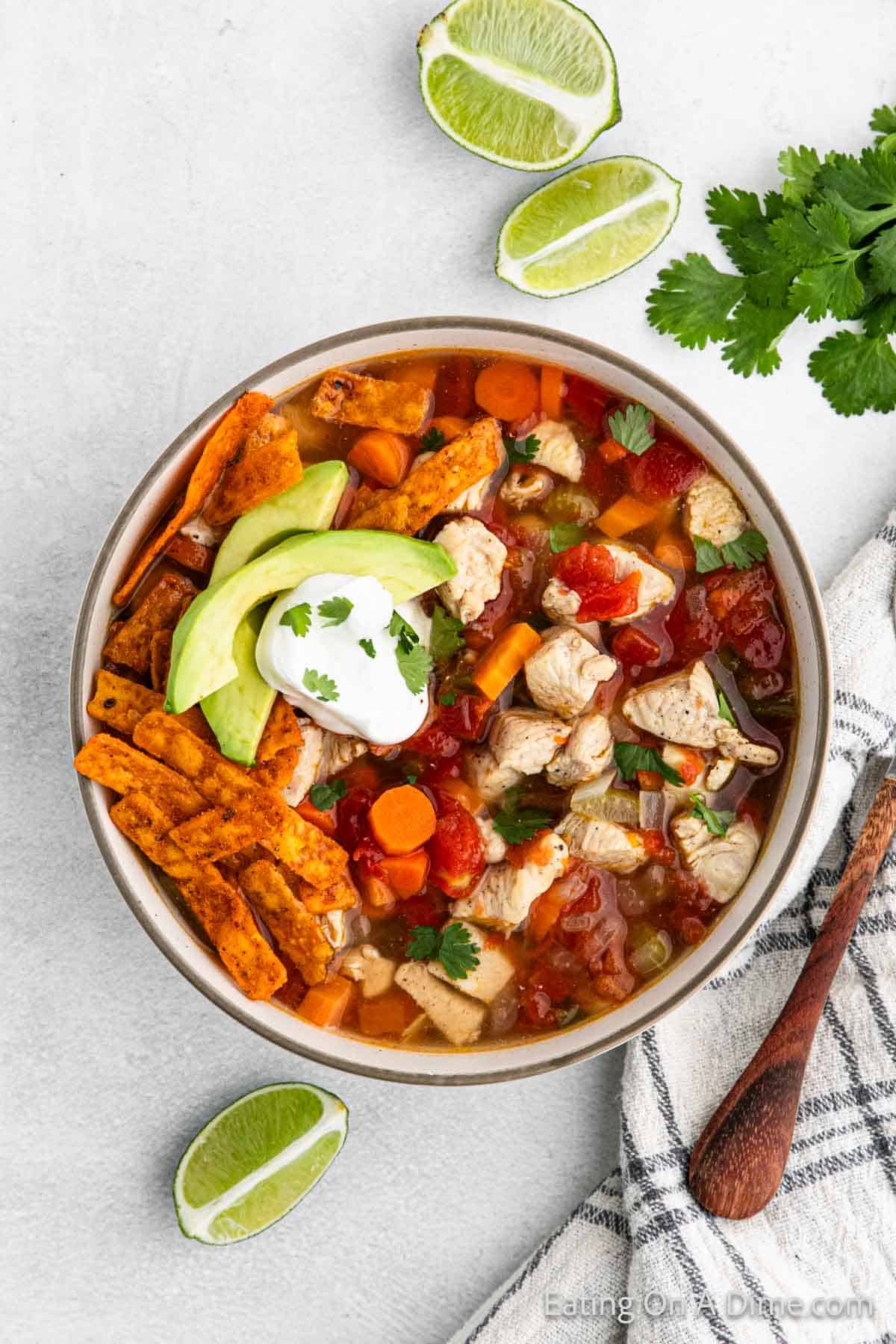 Mexican Chicken Soup in a bowl topped with tortilla strips, slice avocado, and sour cream