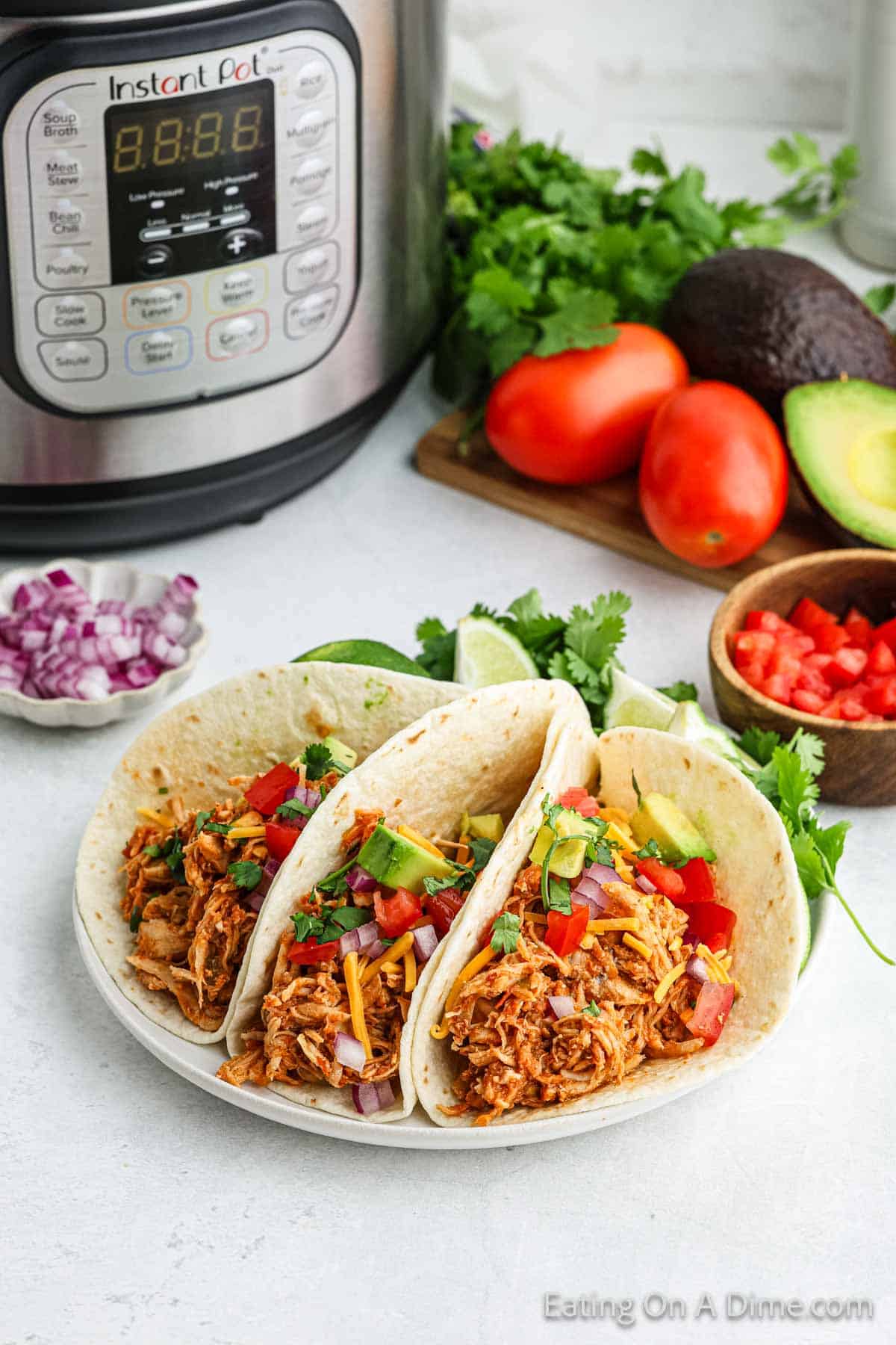 Chicken Tacos on a plate topped with diced avocado, diced tomatoes and red onions