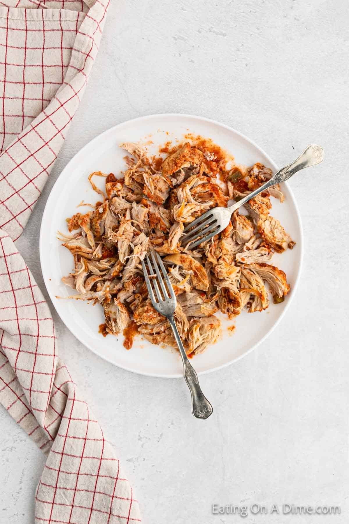 Shredding cooked chicken on a plate with two forks