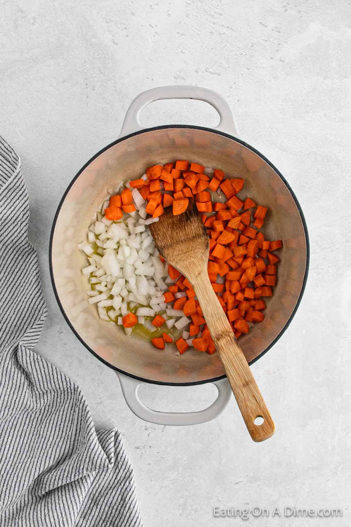 Cooking diced carrots and onions in melted butter in a Dutch Oven with a wooden spoon