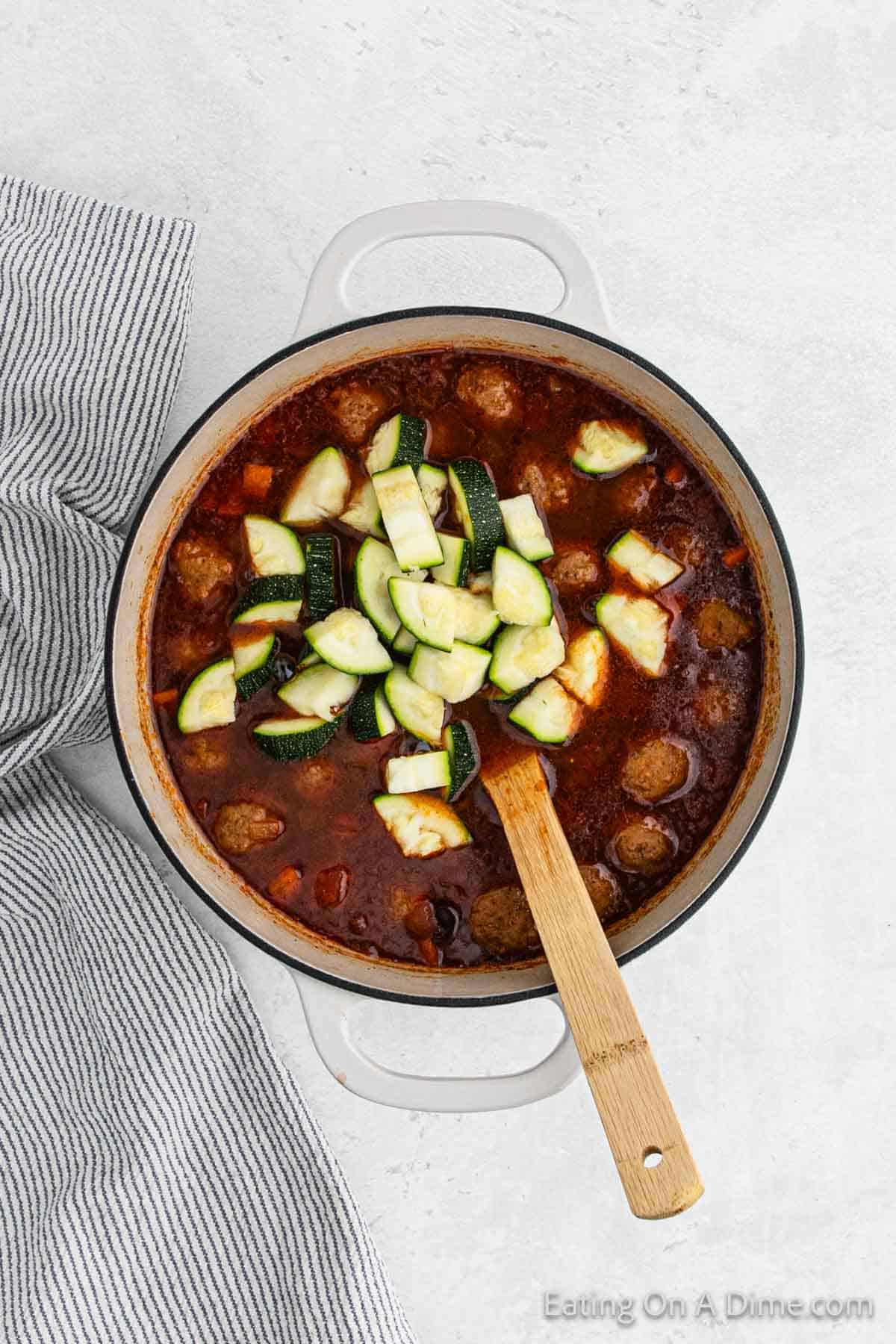 Topping the soup with diced zucchini in the large pot with wooden spoon