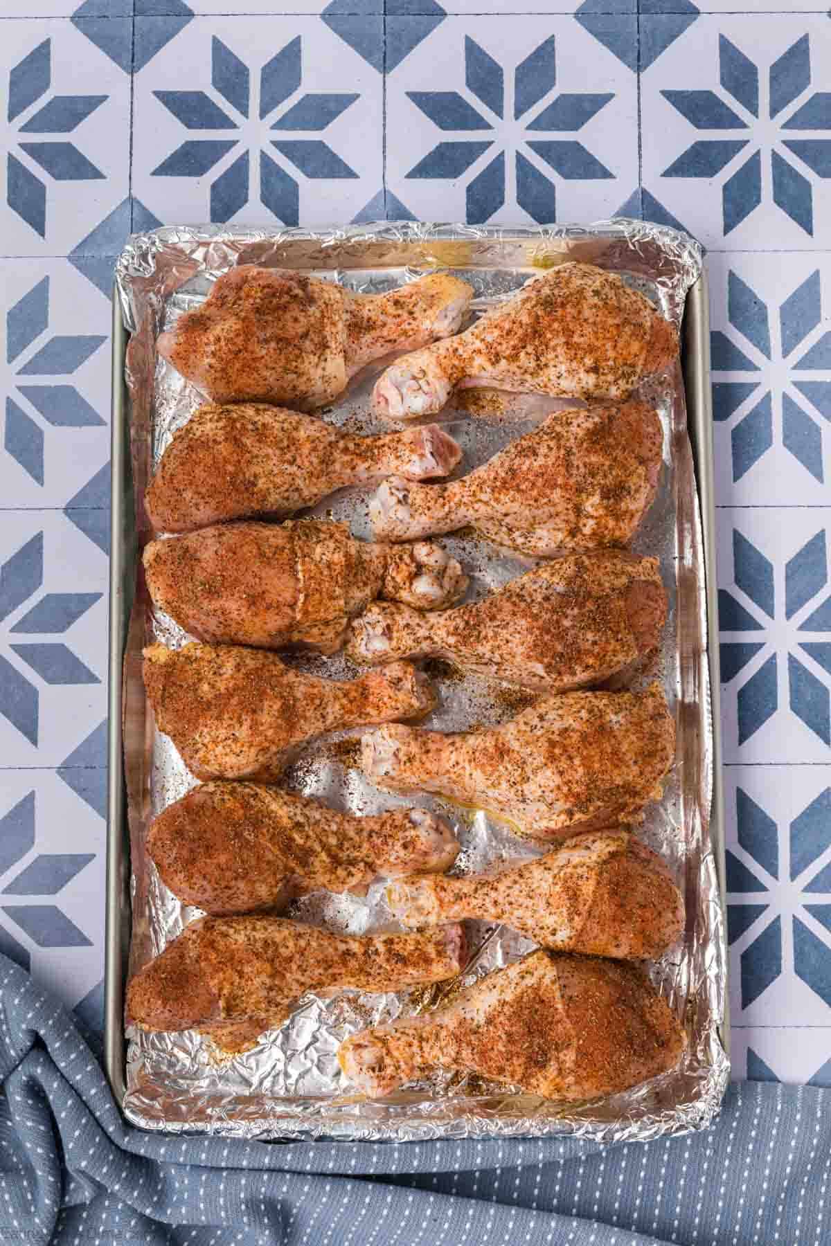 Seasoned chicken drumsticks on a baking sheet lined with foil